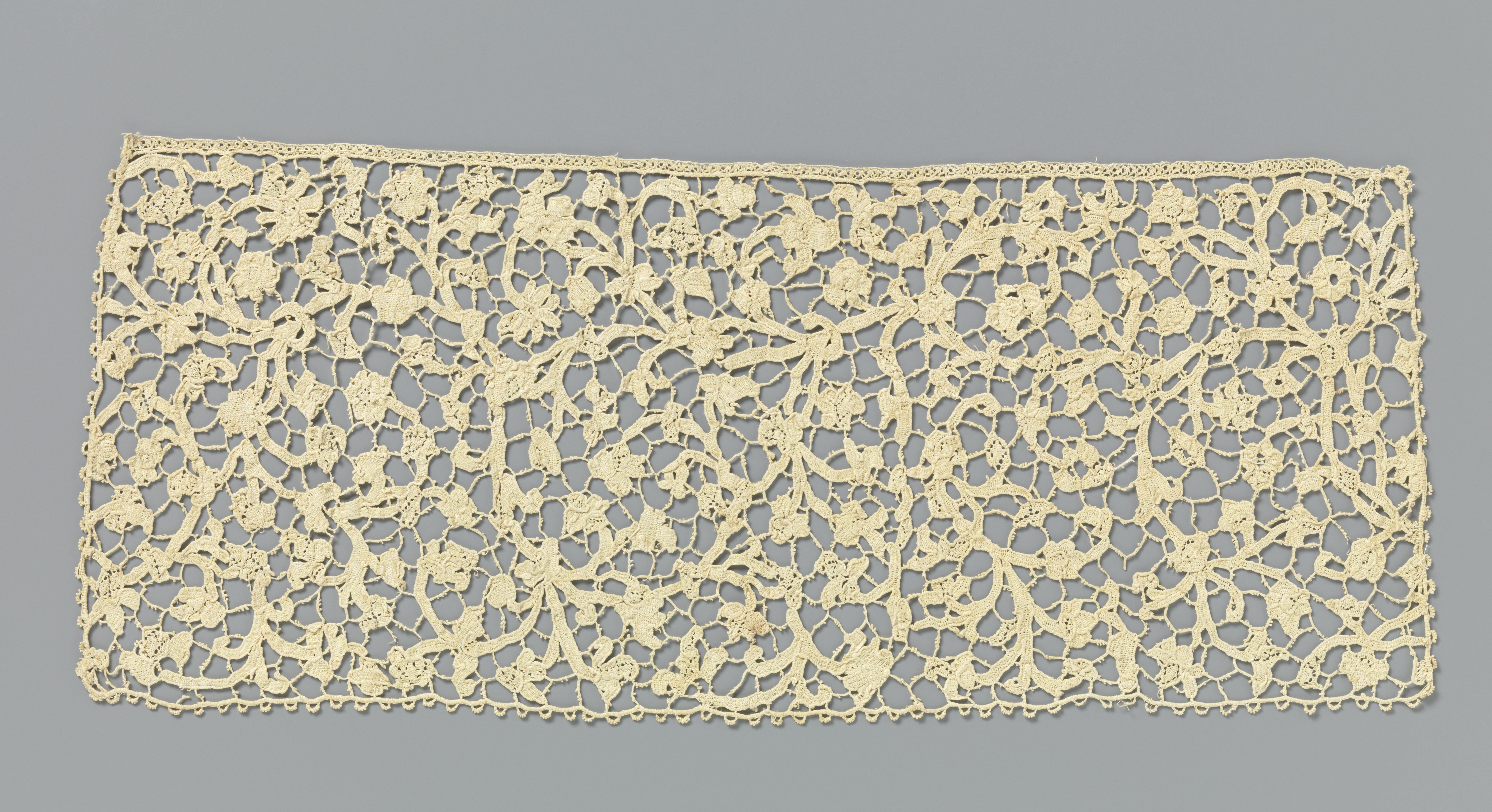 Dasslip van naaldkant met symmetrisch patroon van vele ranken met kleine bladeren en bloemen