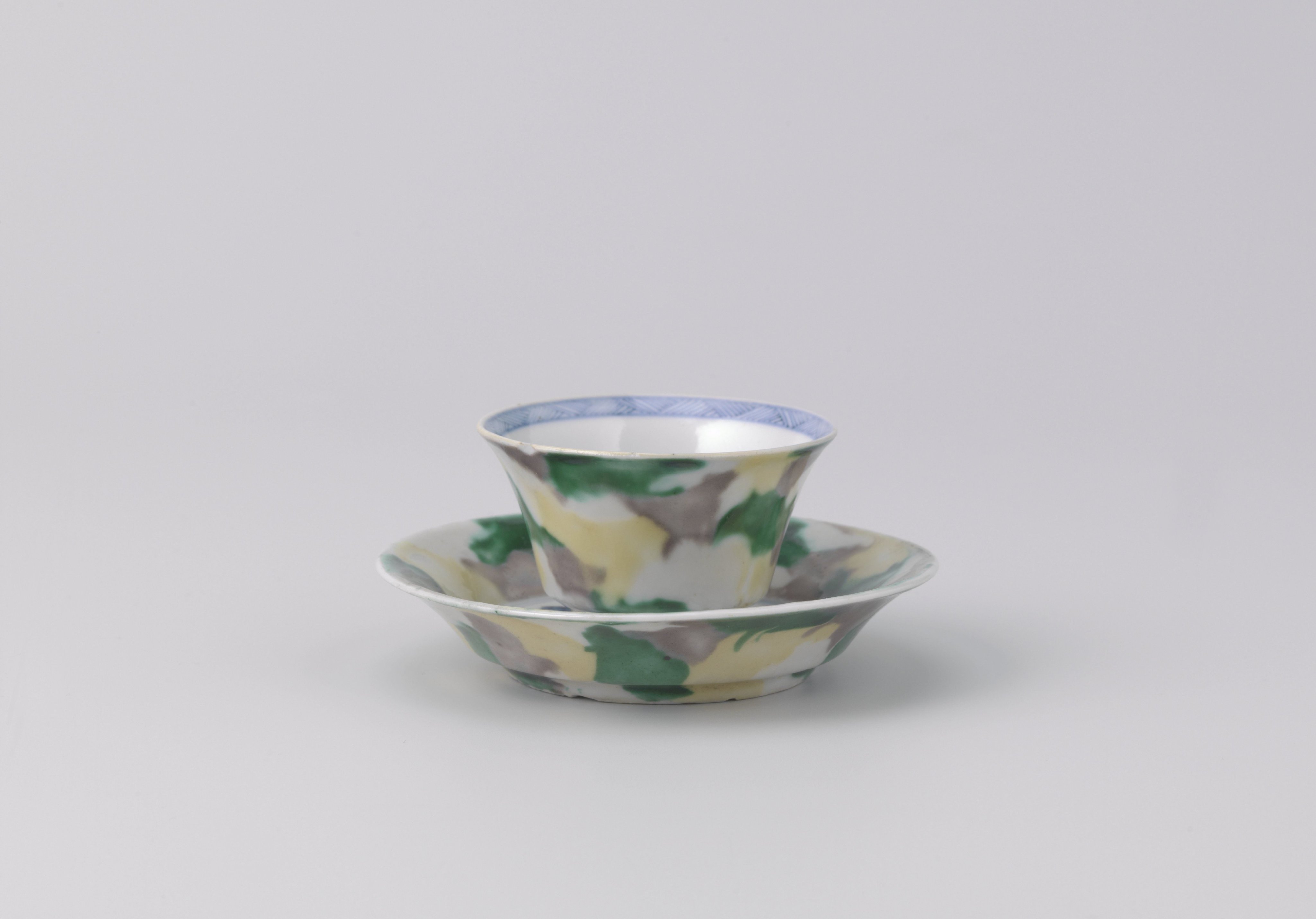 Cup and saucer with 'egg and spinach' pattern and cock among plants