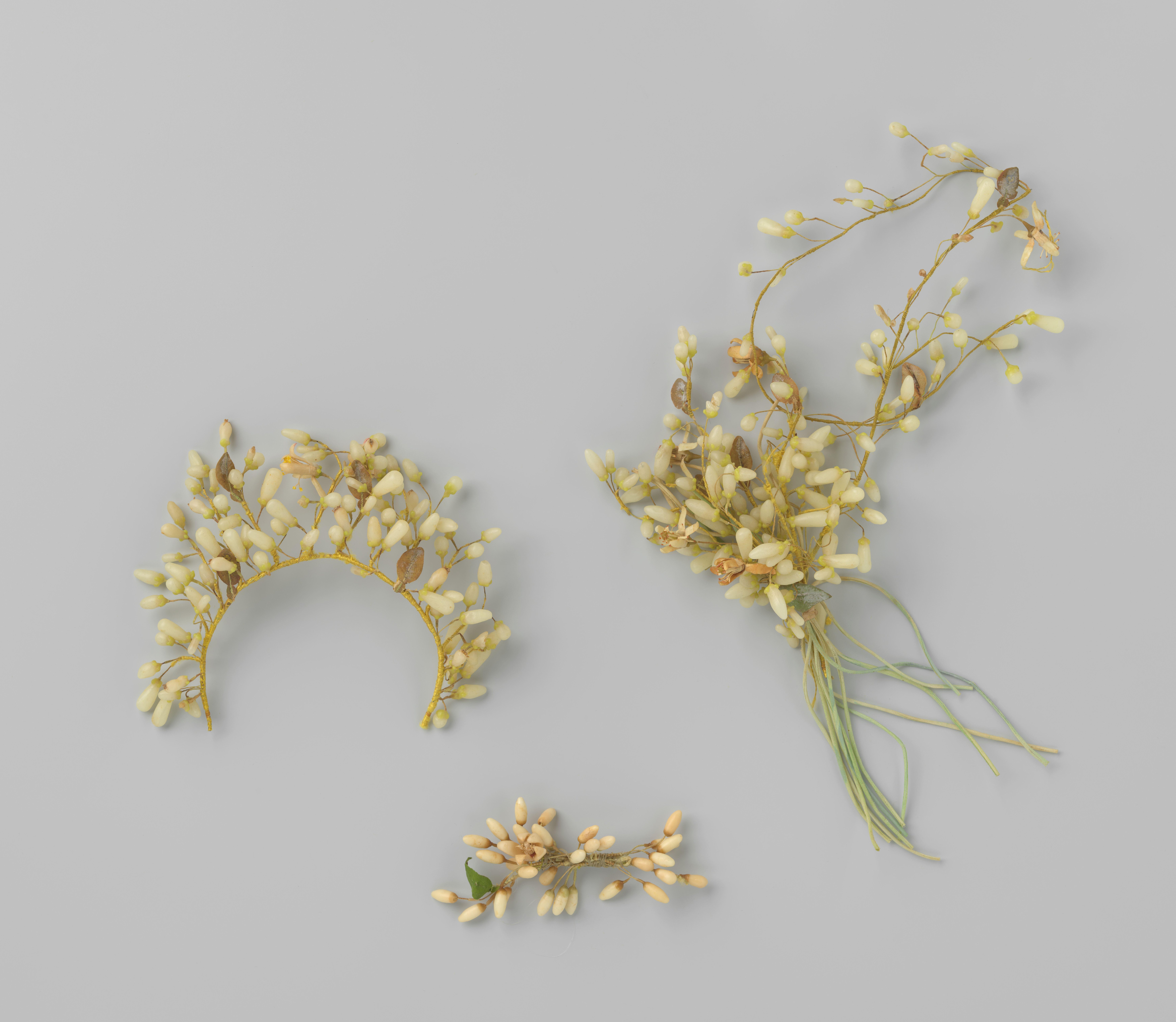Corsage van oranjebloesemknopjes met groene stoffen steeltjes waarvan een lange steel met laiton afhangt