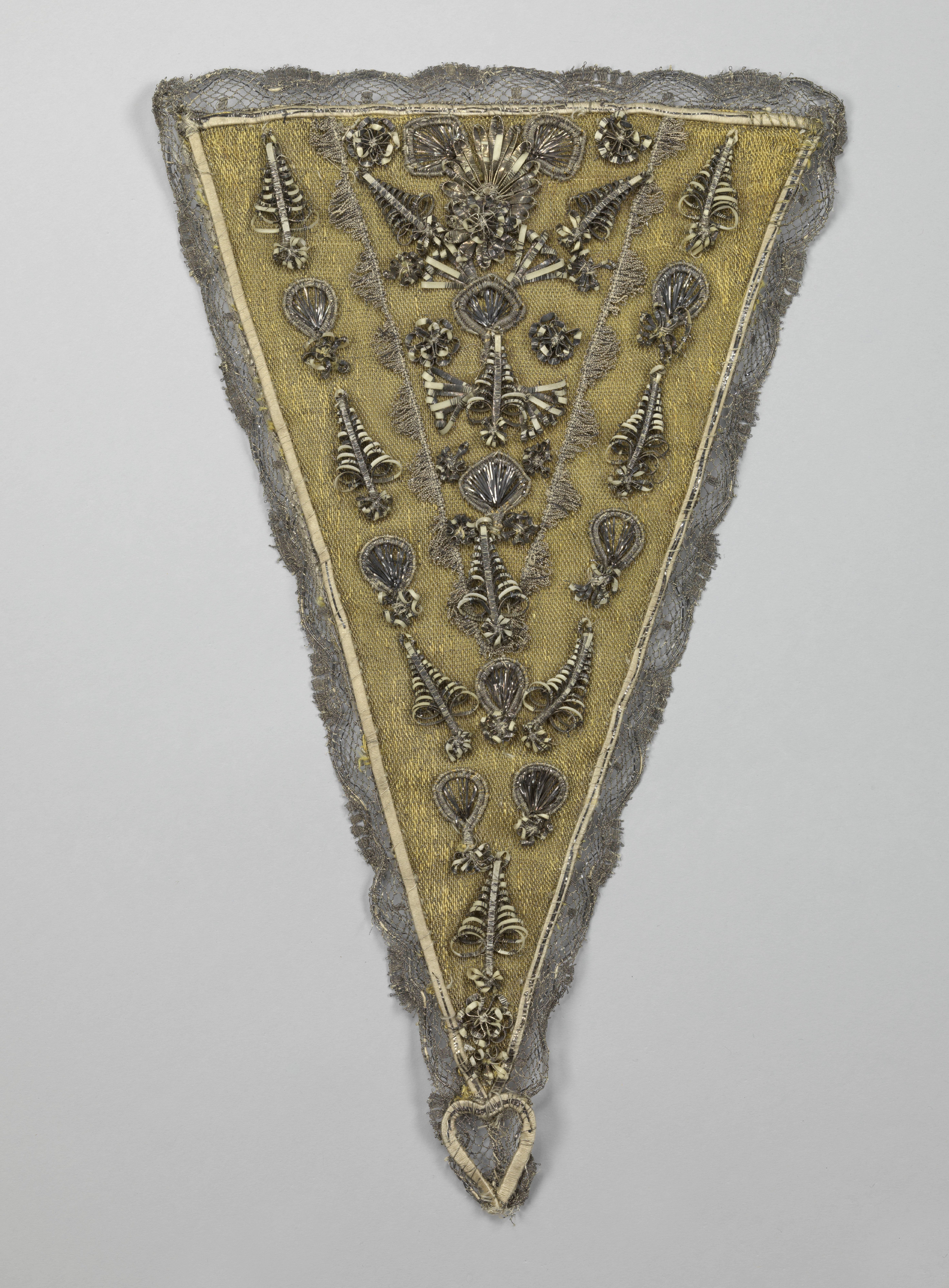 Devant-de-gorge of driehoekig borststuk van zilverbrokaat tussen gele zijden linten bedekt met zilveren tulen passement, beide versierd met ornamenten van (oorspronkelijk verguld) bladzilver over perkament en afgezet met een geschulpte rand van zilveren tule, zijden appliques, zijden chenille, strikken van (oorspronkelijk verguld) bladzilver en zilverdraad