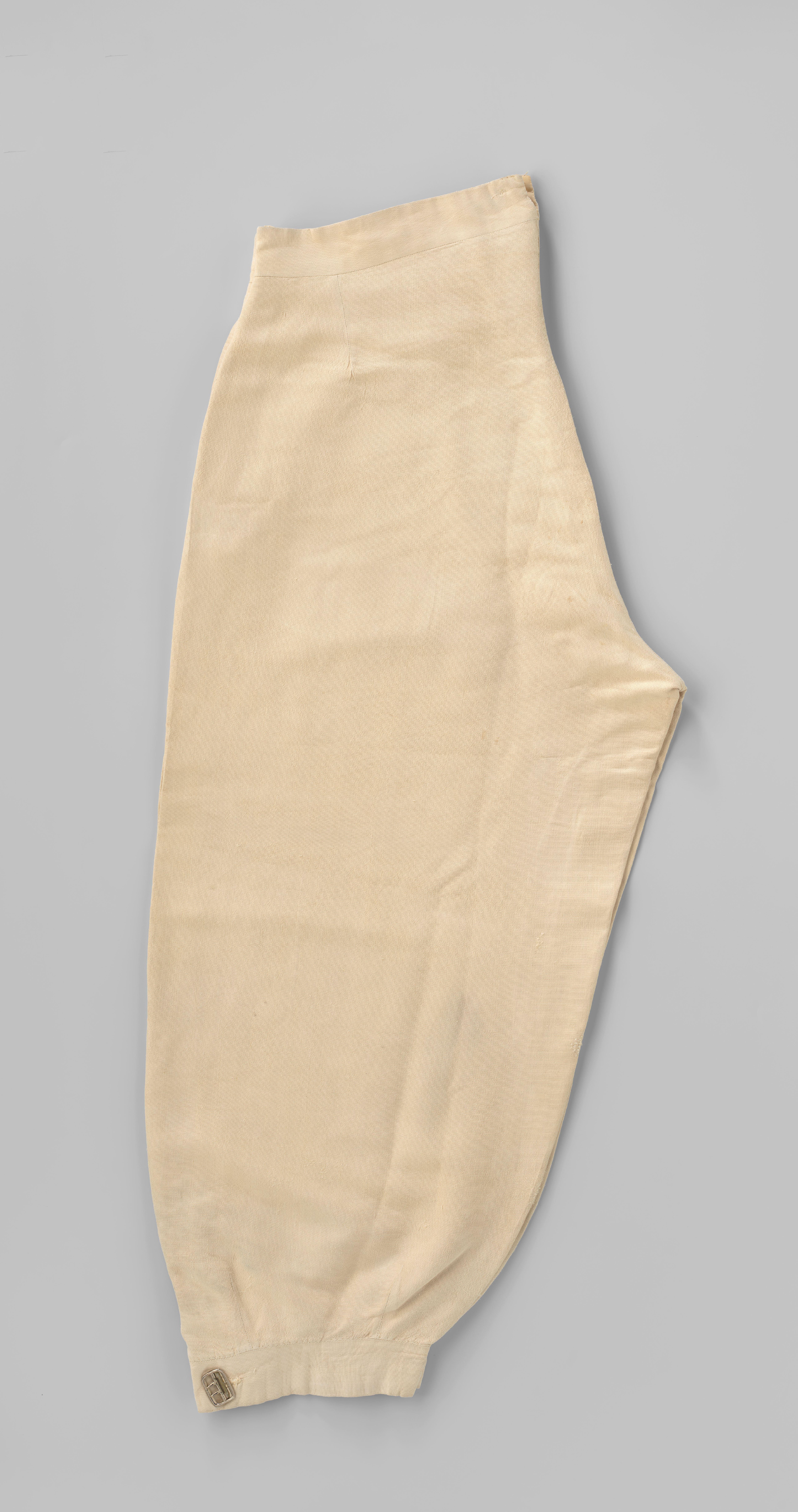 Broek in plus-fourmodel van beige katoen, met steekzakken in de zijnaden, gulp met benen knopen, onderaan een gespsluiting en aan de binnenkant van de taille acht knopen