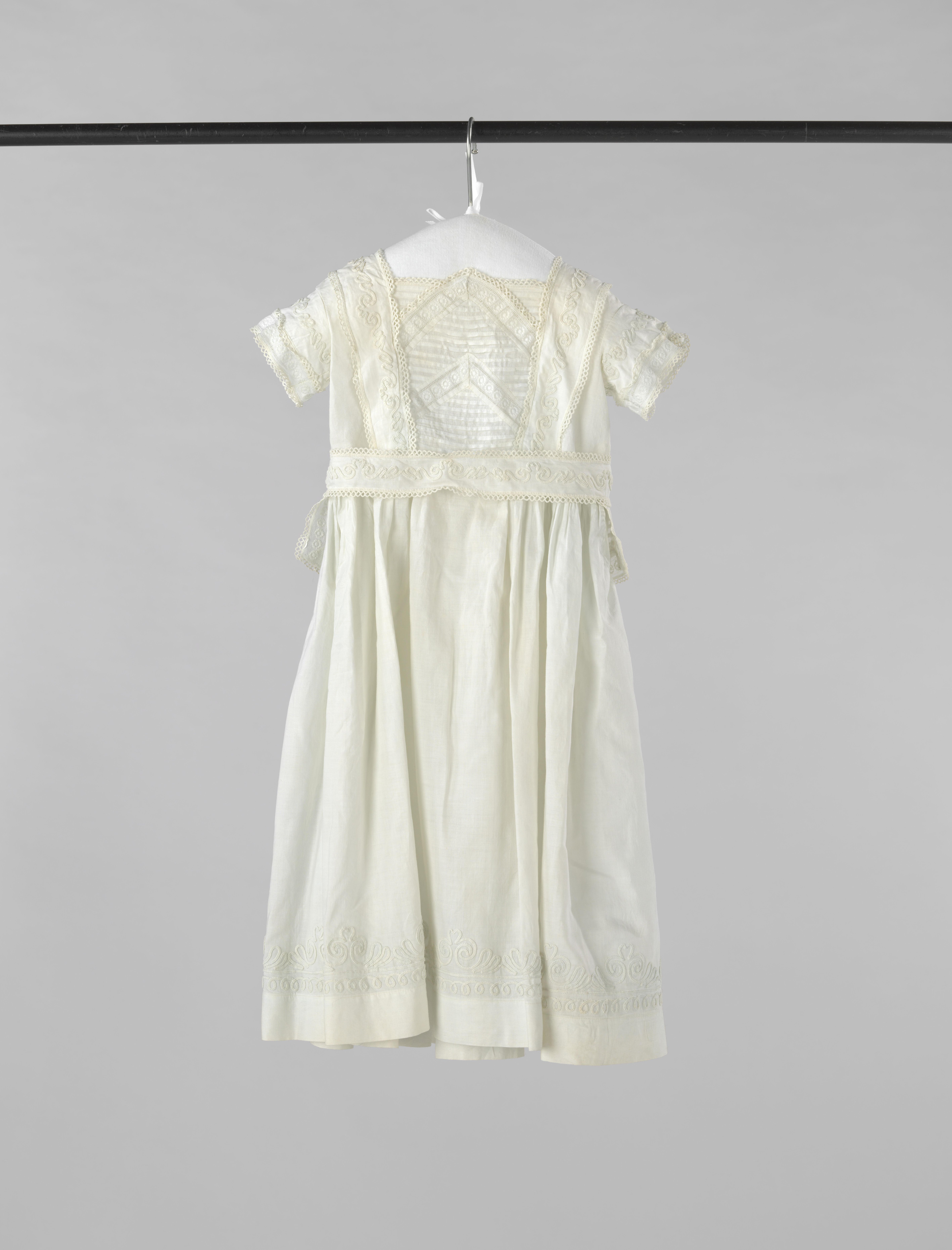 Kinderjurk van wit linnen met soutache en tussenzetsels, met ceintuur