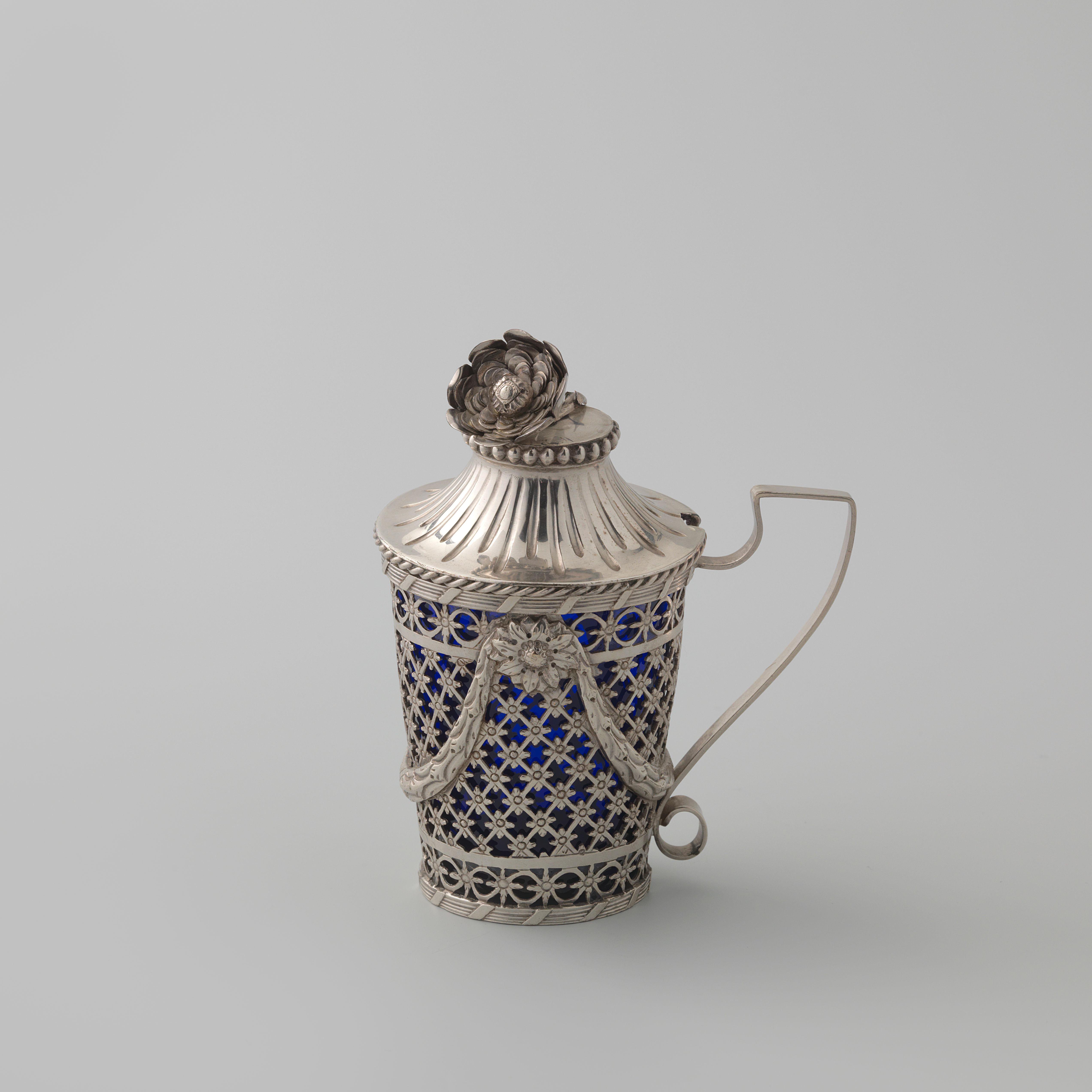 Mosterdpot van zilver, rond en naar boven uitlopend met gezaagd rasterwerk met bloemrozetten en geappliqueerde guirlandes; binnenbak van blauw glas