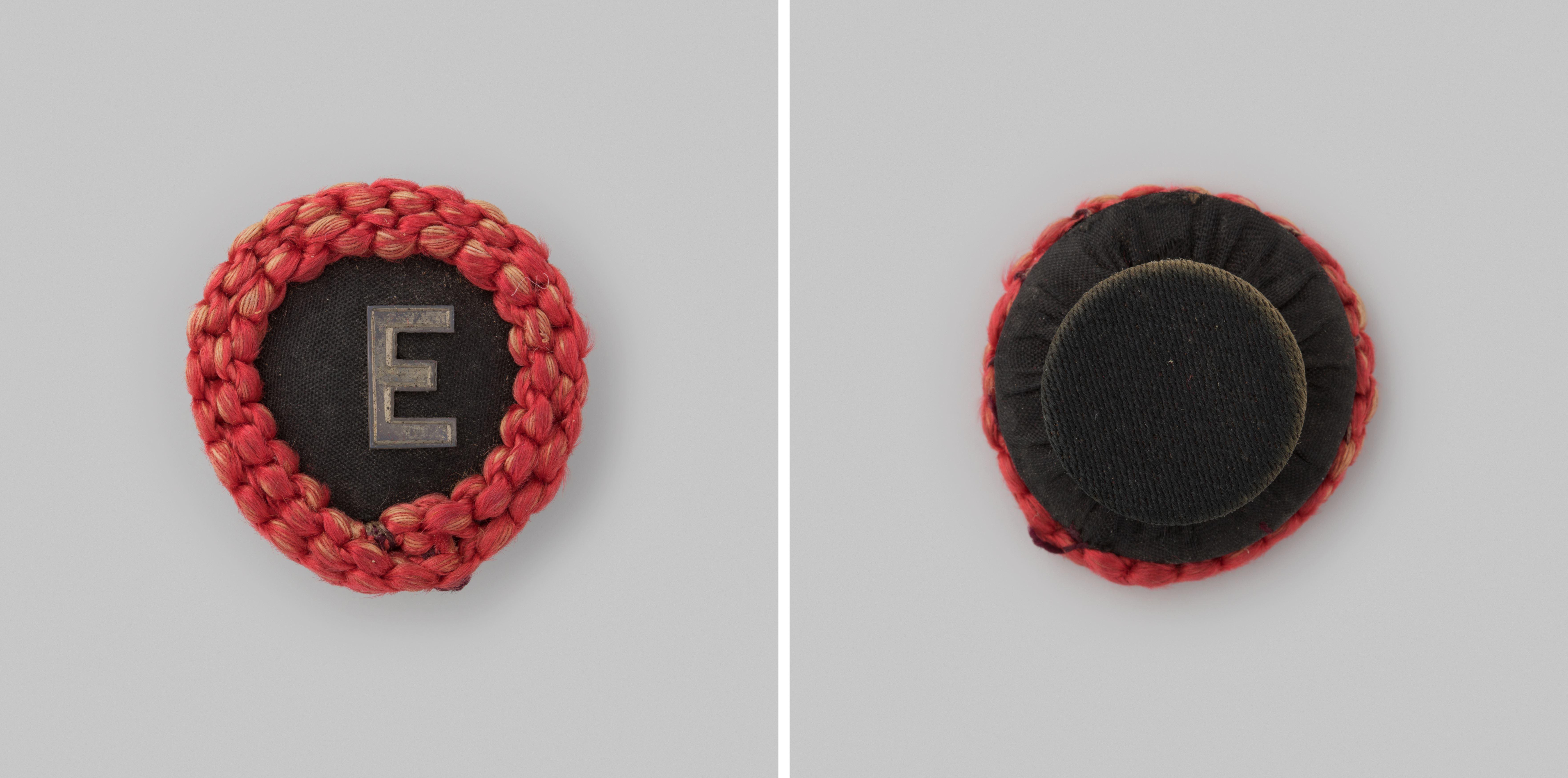 Draagteken van de vereniging Eendragt in de vorm van een zwarte knoop met een geslagen zilveren E, om de knop een dubbele rij van gevlochten rood koord