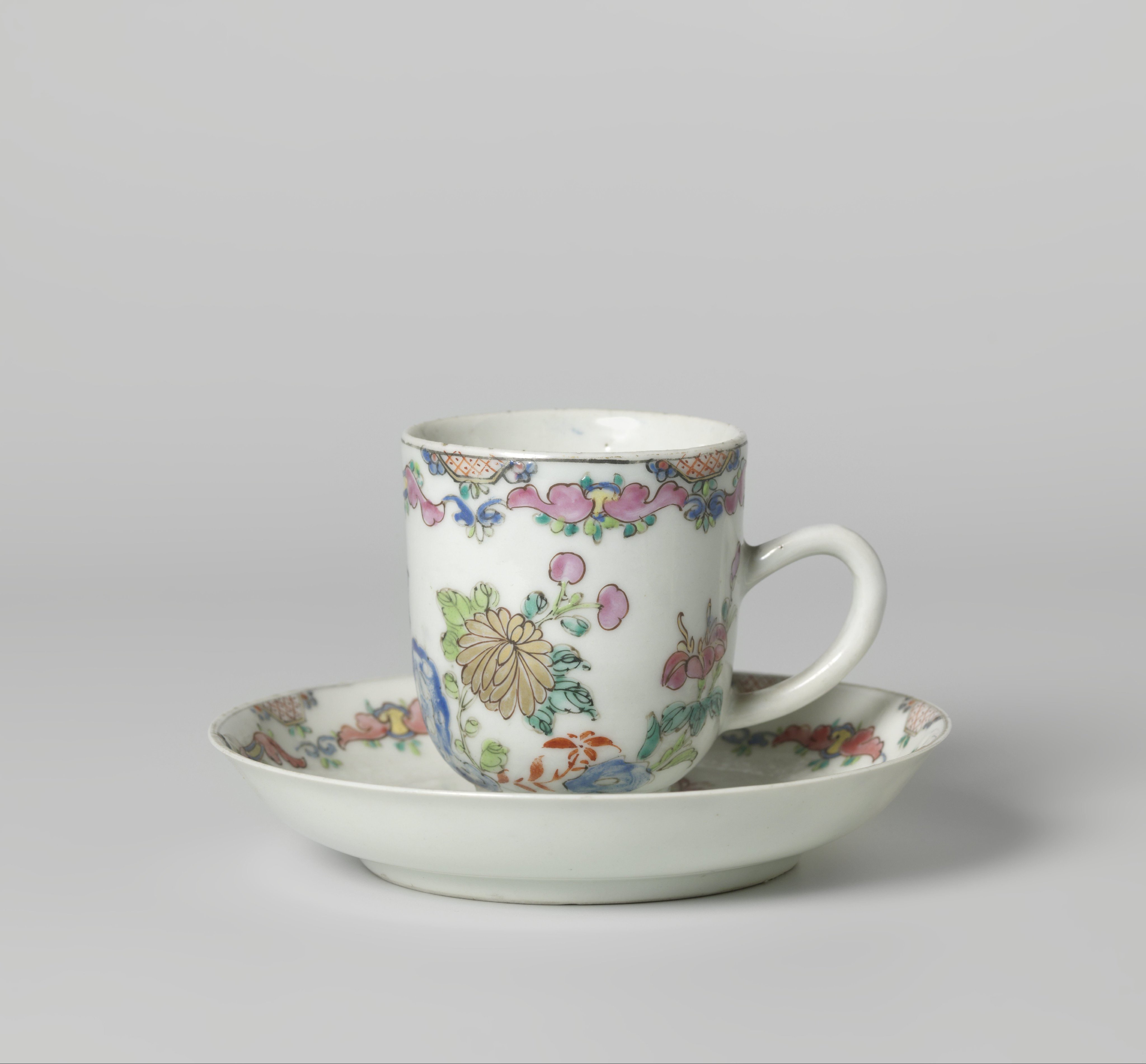 Chocolate cup and saucer with flowering plants near a rock and scrolls