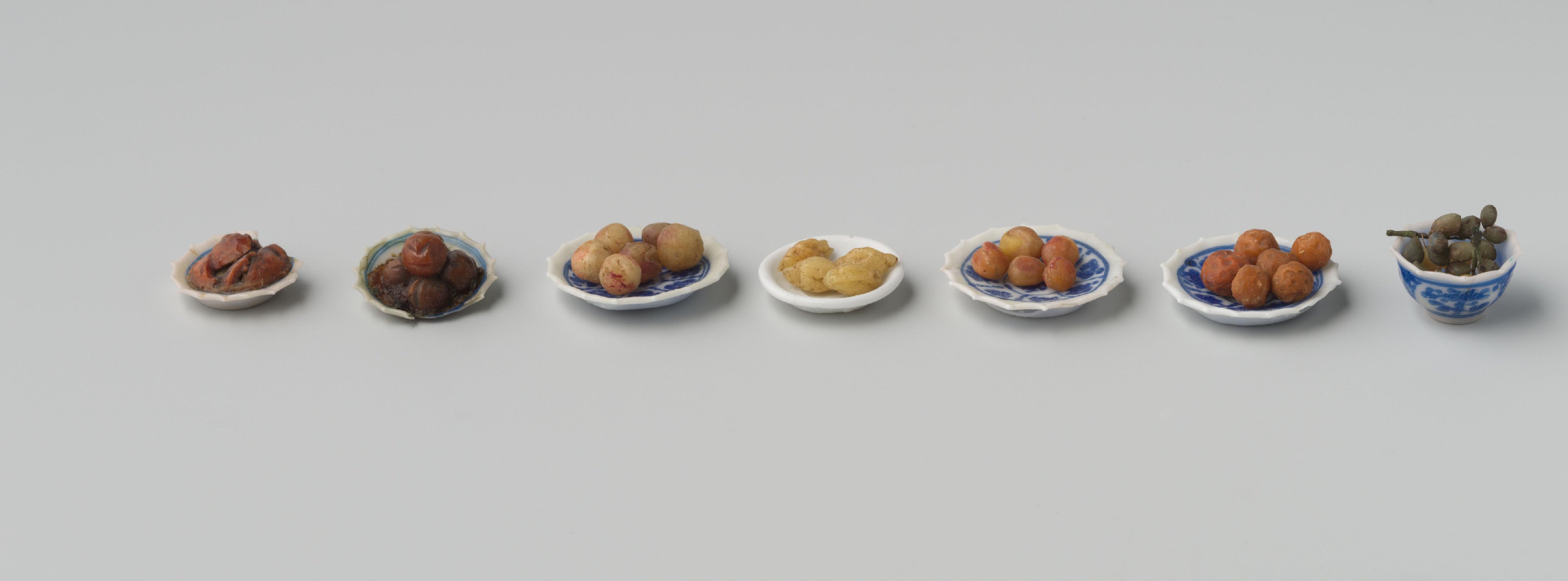 Diverse vruchten, vervaardigd van was, waaronder 6 sinaasappels, 4 citroenen, 5 perziken, 5 appels, 4 pruimen, 1 peer en 2 druiventrosjes.