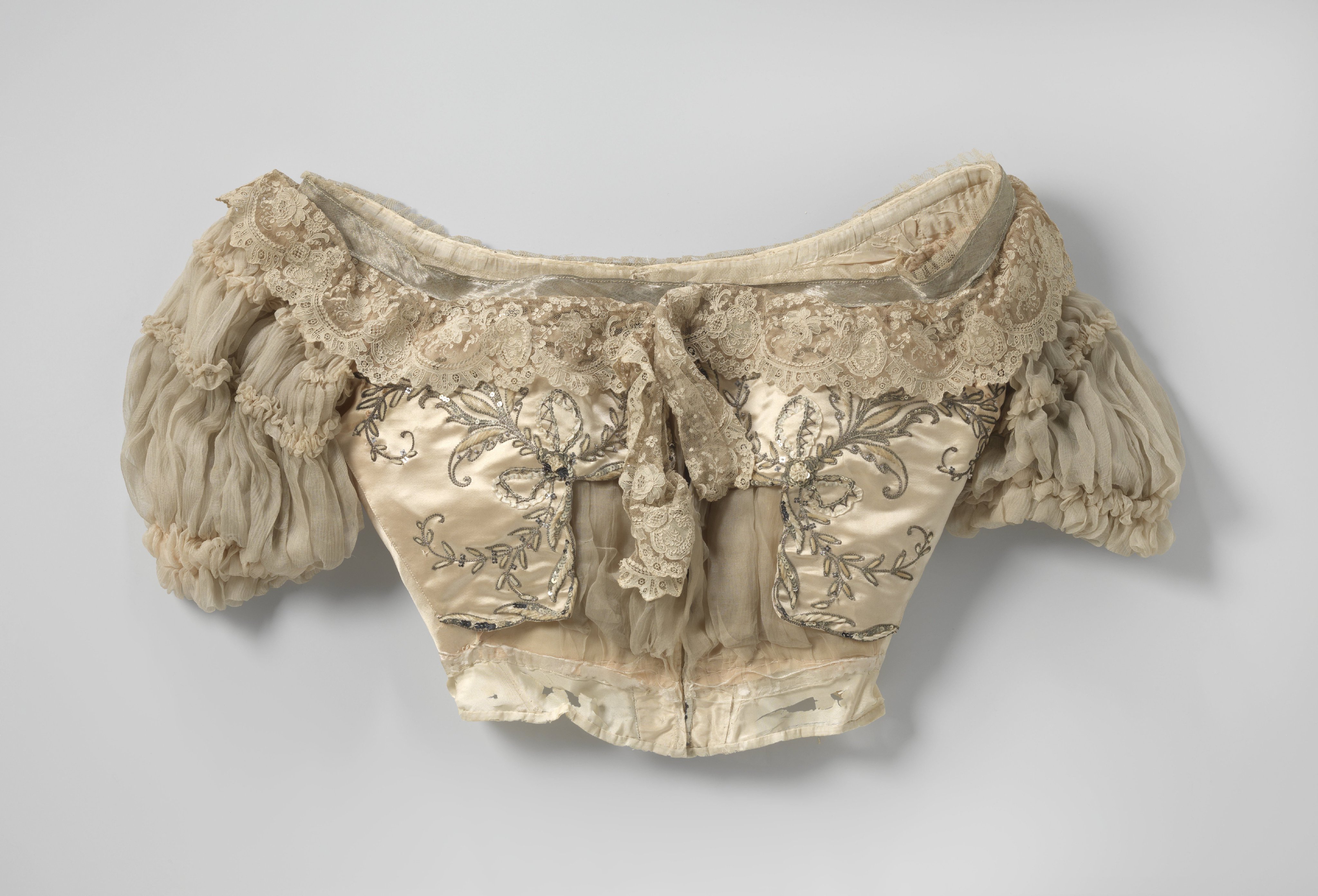Lijf met lage hals en pofmouwen van zalmkleurige satijn, versierd met rank- en kandelaberornament van zilverdraad, lovers, chenille en zijde