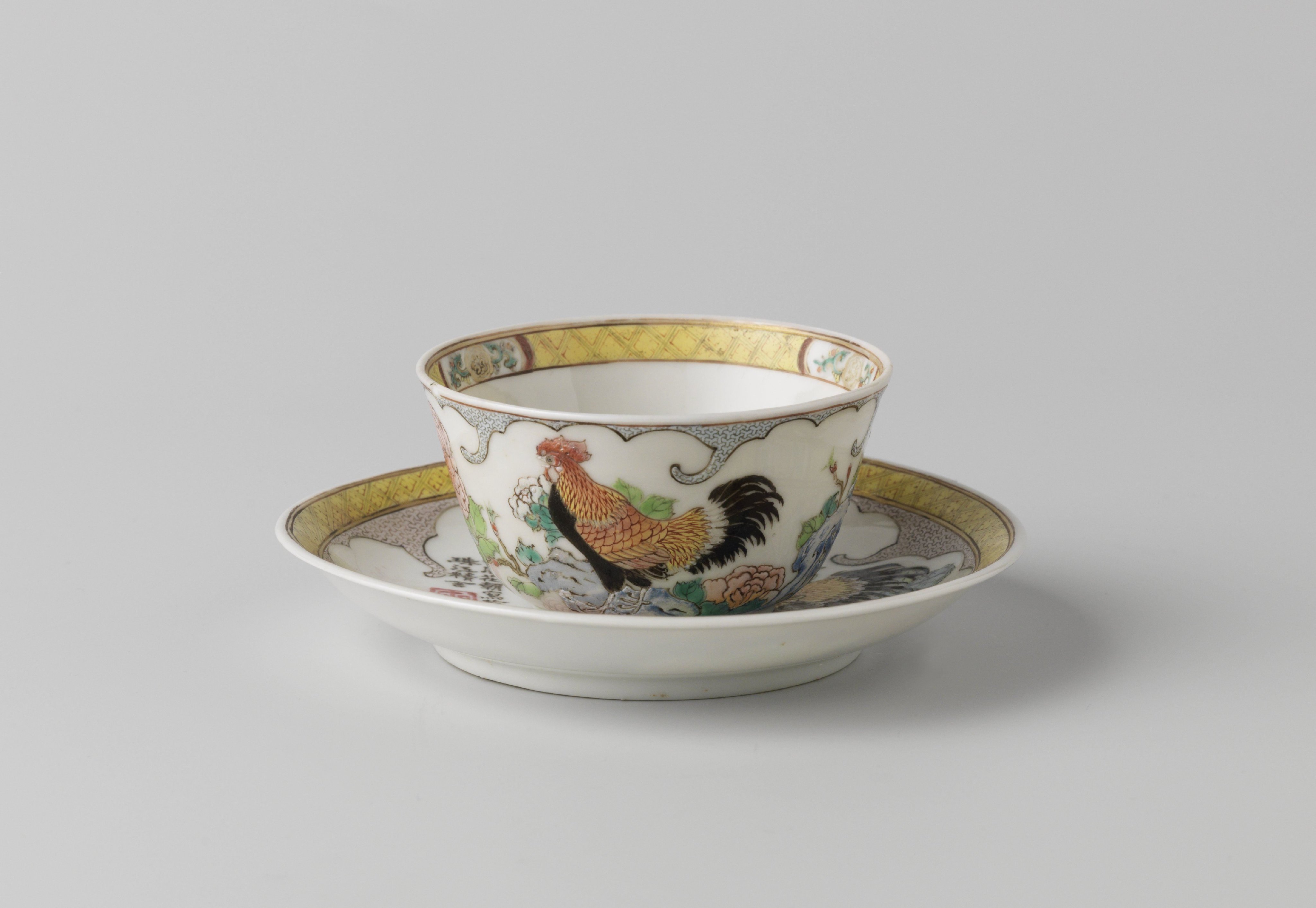 Bell-shaped cup and saucer with a cock on a rock with flowering plants