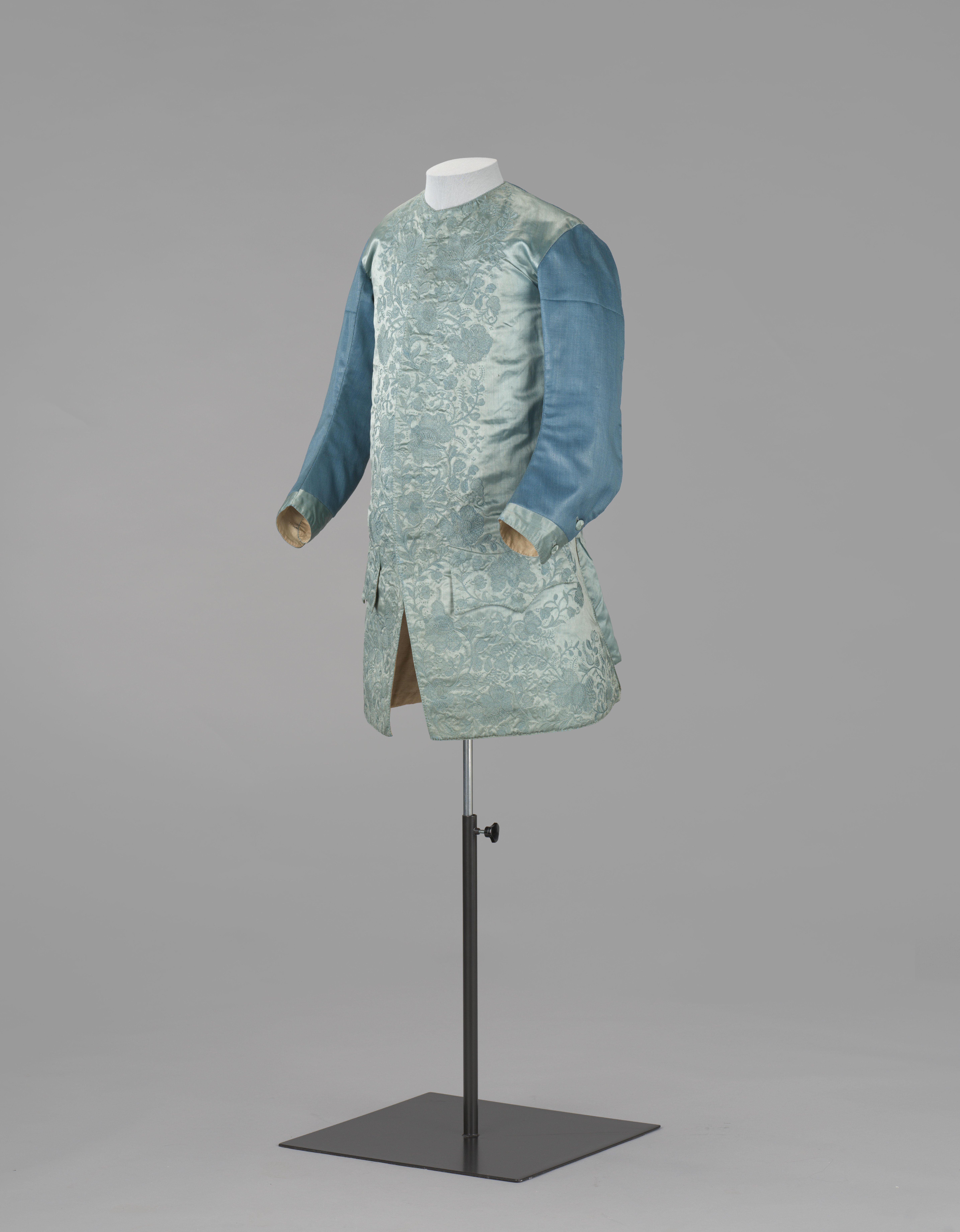 Vest met blinde sluiting, waaronder twaalf knopen van zijdedraad, van lichtblauw satijn, in blauw geborduurd met florale motieven; lange mouwen en rug van gecalandeerd kamelot