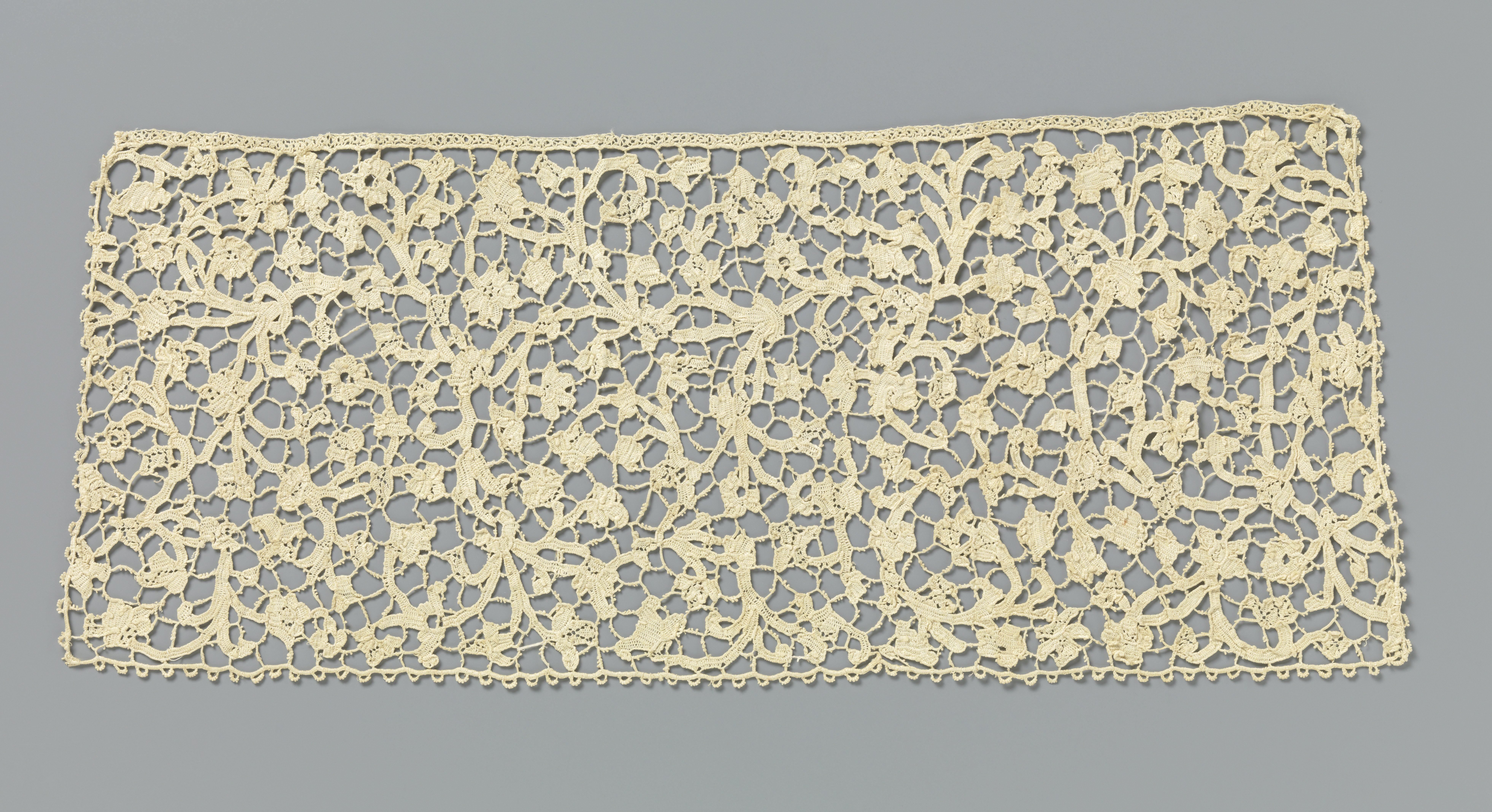 Dasslip van naaldkant met symmetrisch patroon van vele ranken met kleine bladeren en bloemen