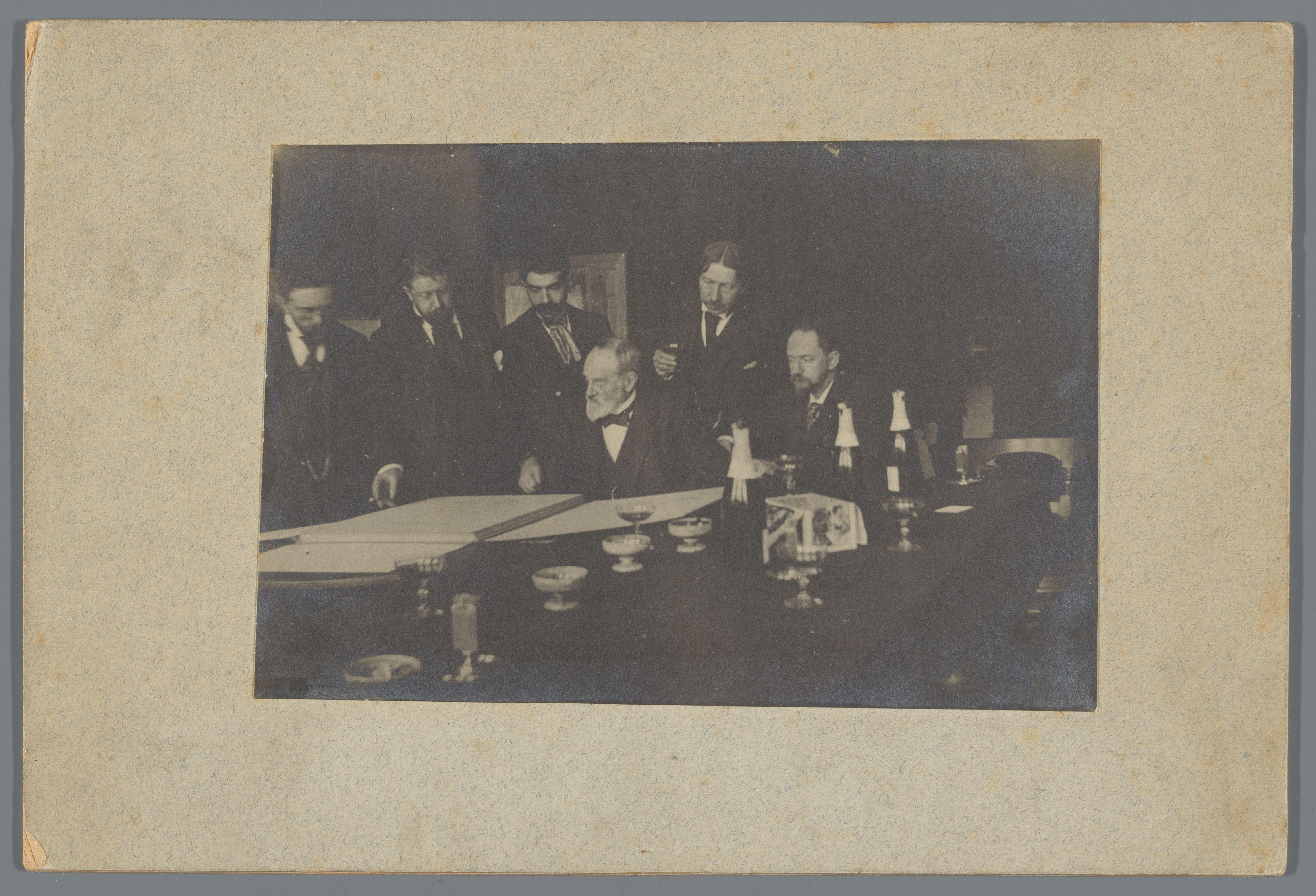 George Hendrik Breitner en anderen, een portefeuille bekijkend, mogelijk tijdens een kunstbeschouwing bij Arti et Amicitiae