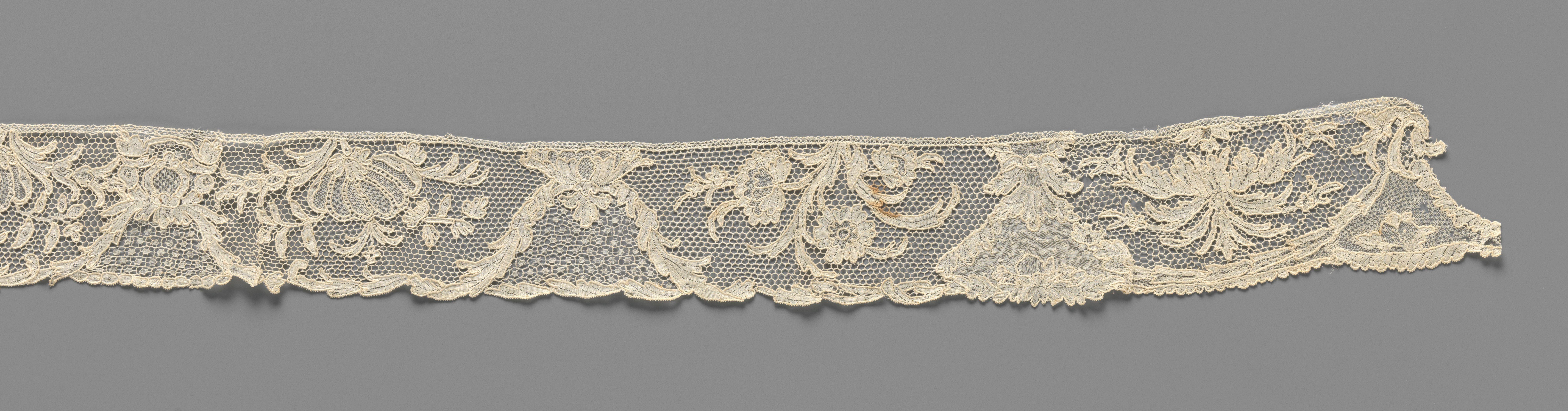 Strook naaldkant met symmetrische compositie van klokvormige velden gevormd door acanthusbladeren en grote bloemen