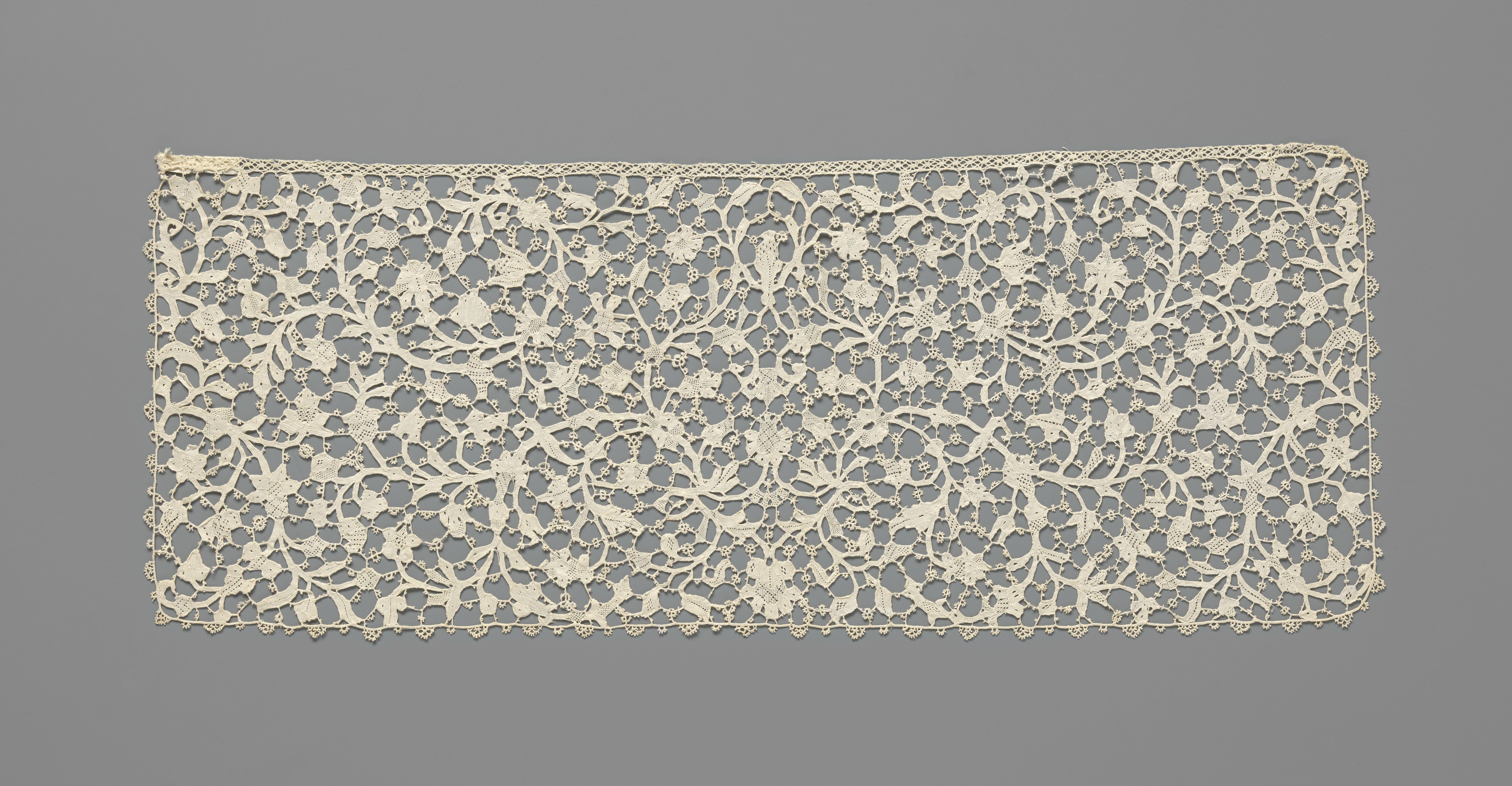 Slip van naaldkant met een symmetrisch patroon van dunne omkrullende ranken met veelsoortige bloemen