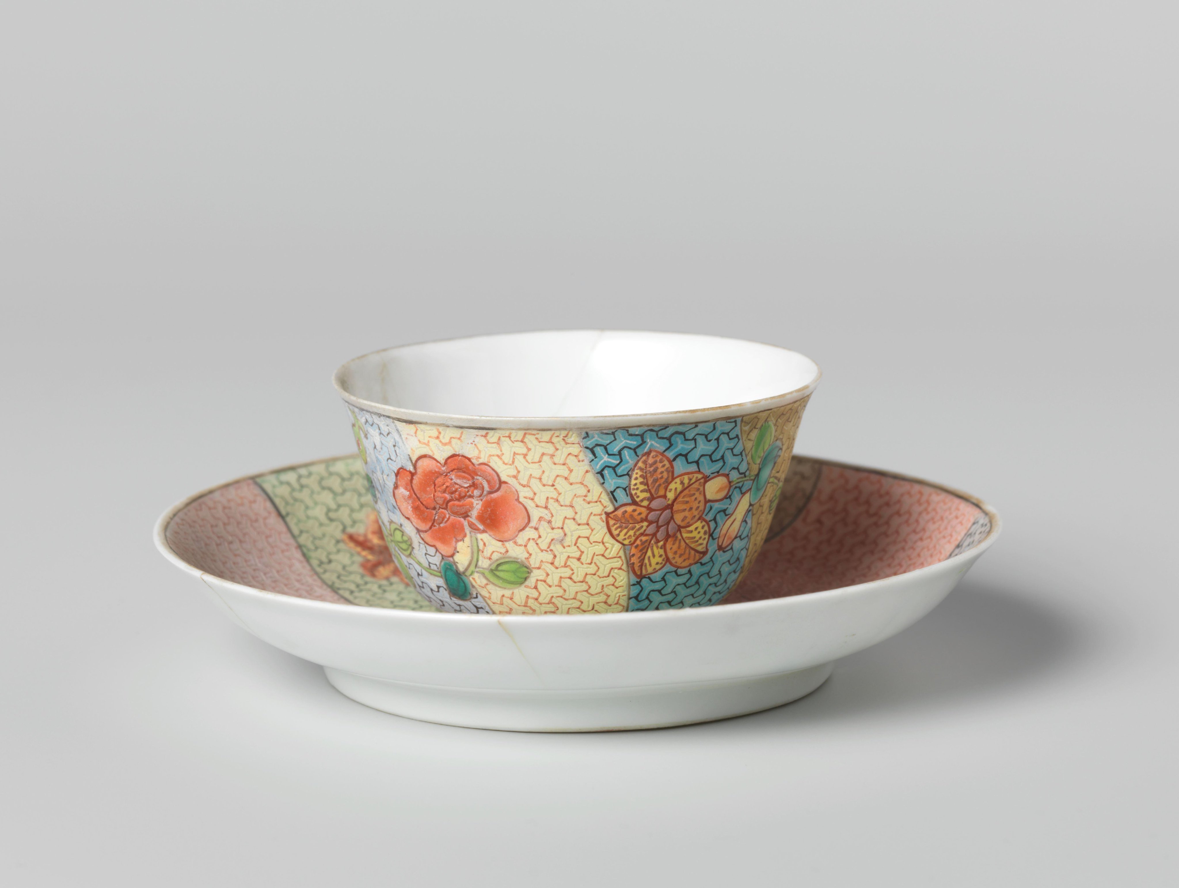 Bell-shaped cup and saucer with three flower sprays on multi-colored diaper-pattern