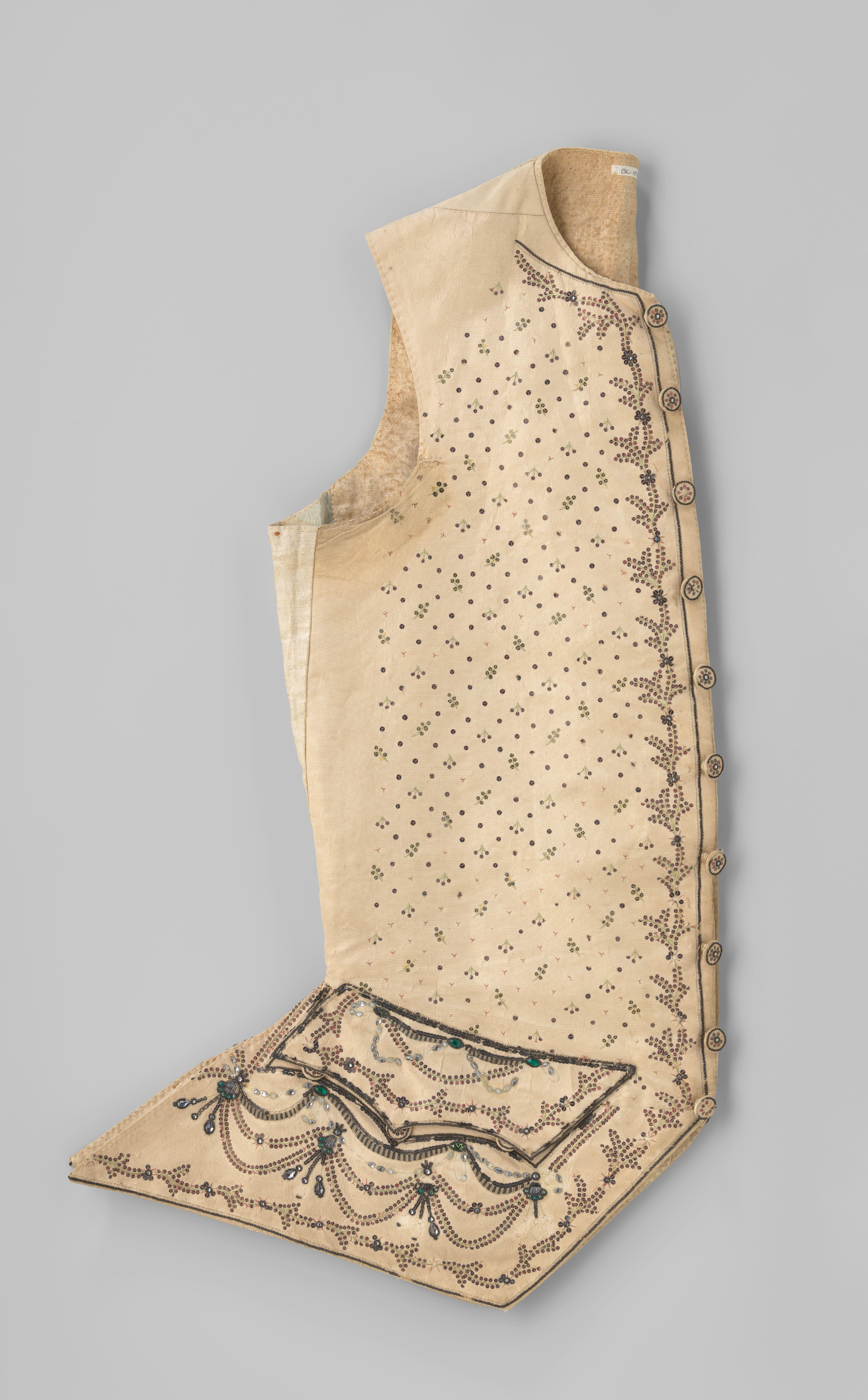 Vest van crème ripszijde, meerkleurig geborduurd met noppen, bloemen, bladranken en lambrequins met pailletten, gekleurde stenen en biezen van metaaldraad; achter wit linnen.