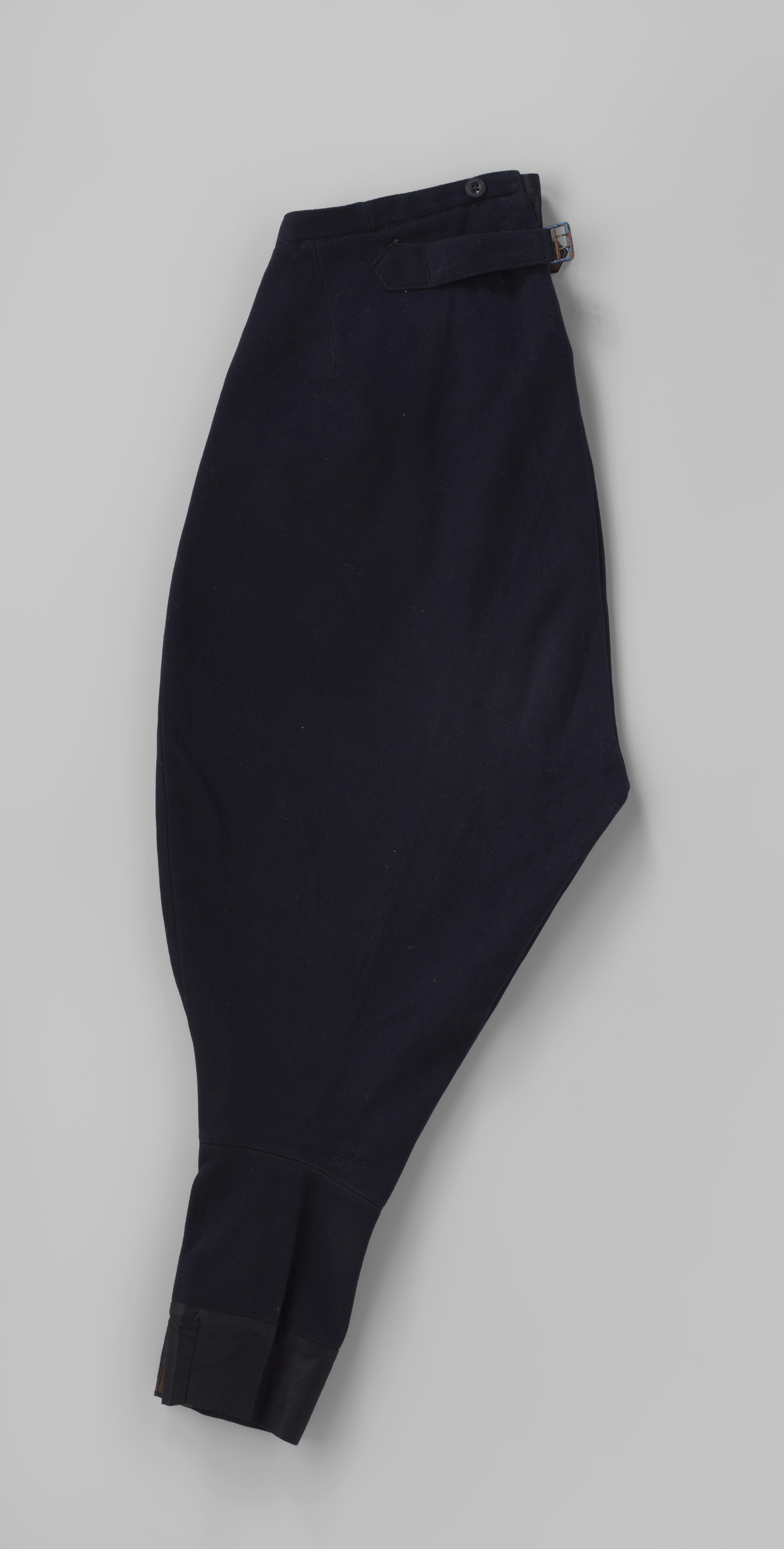 Poffende kuitbroek van zwart laken, met tailleband, hogere rug, gulp met blindsluiting, twee schuine zakken, één klepzak en vanachter banden met gesp; onderdeel chauffeurspak