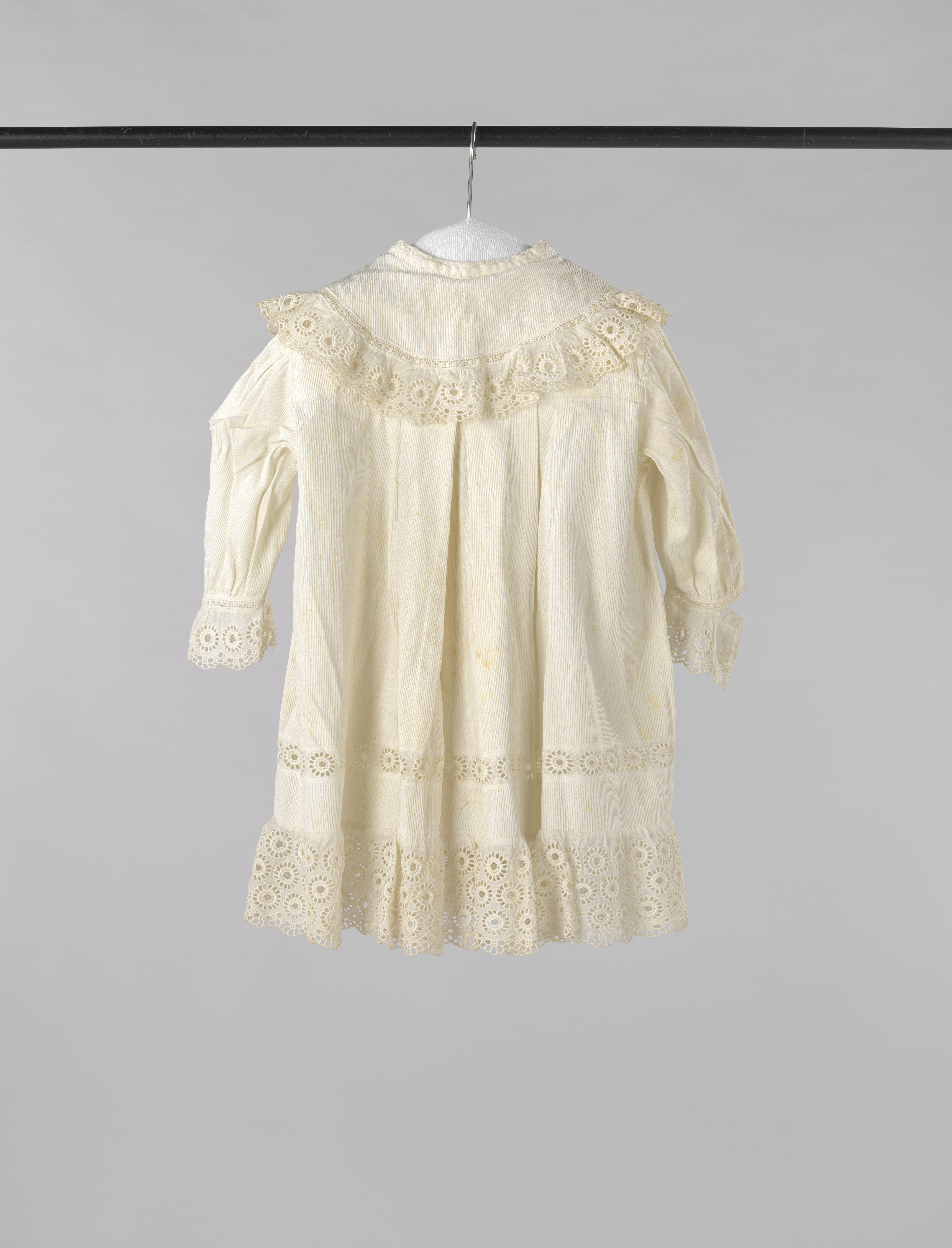 Kinderjasje van wit keperkatoen met afhangende ronde kraag en versierd met broderie anglaise.