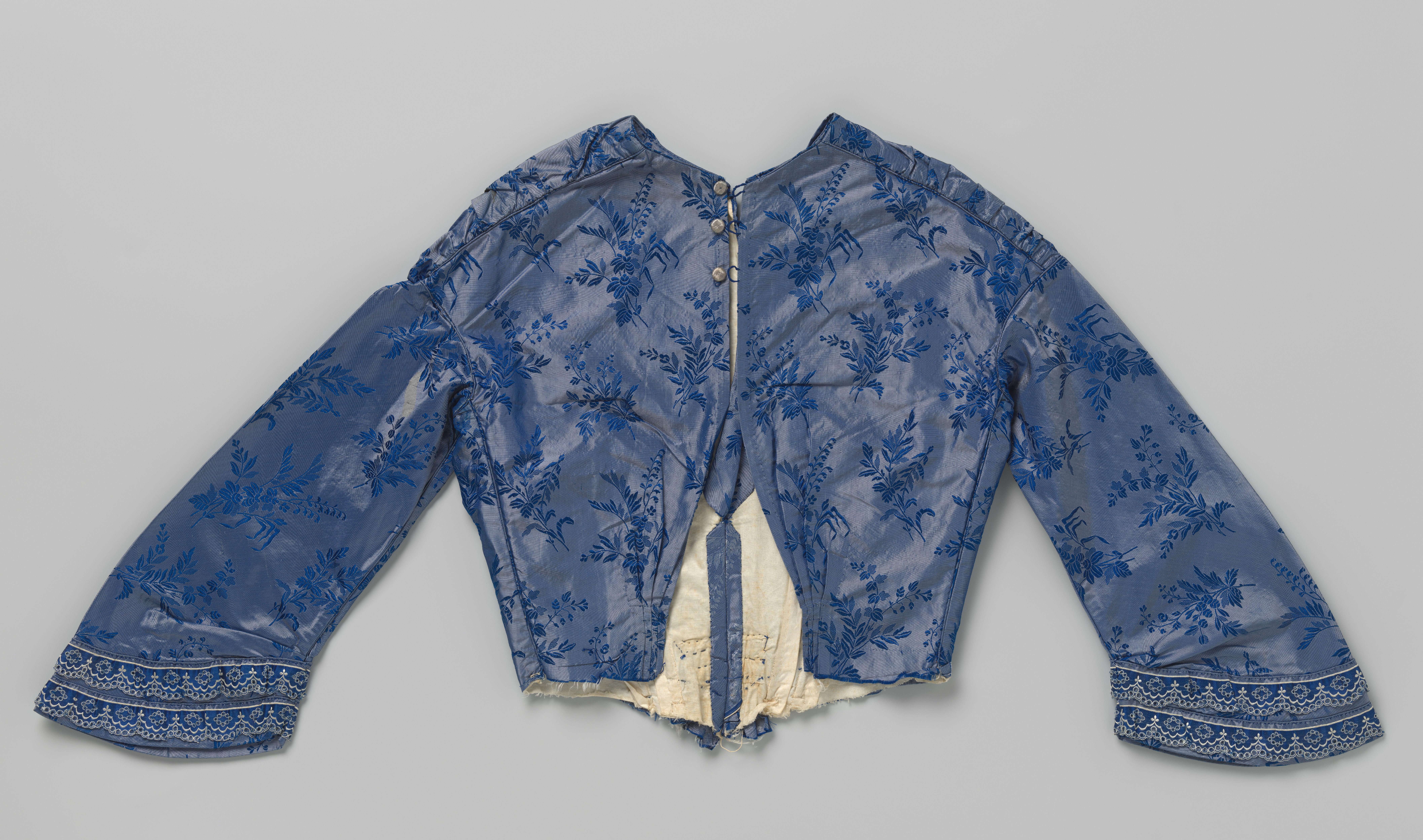 Lijf met lange mouwen en blauwwit passement, diepe V-vormige voorhals, knoopsluiting en geplooid lijf met ingerimpelde schoot, van blauwe changeant tafzijde met bloemtakken.