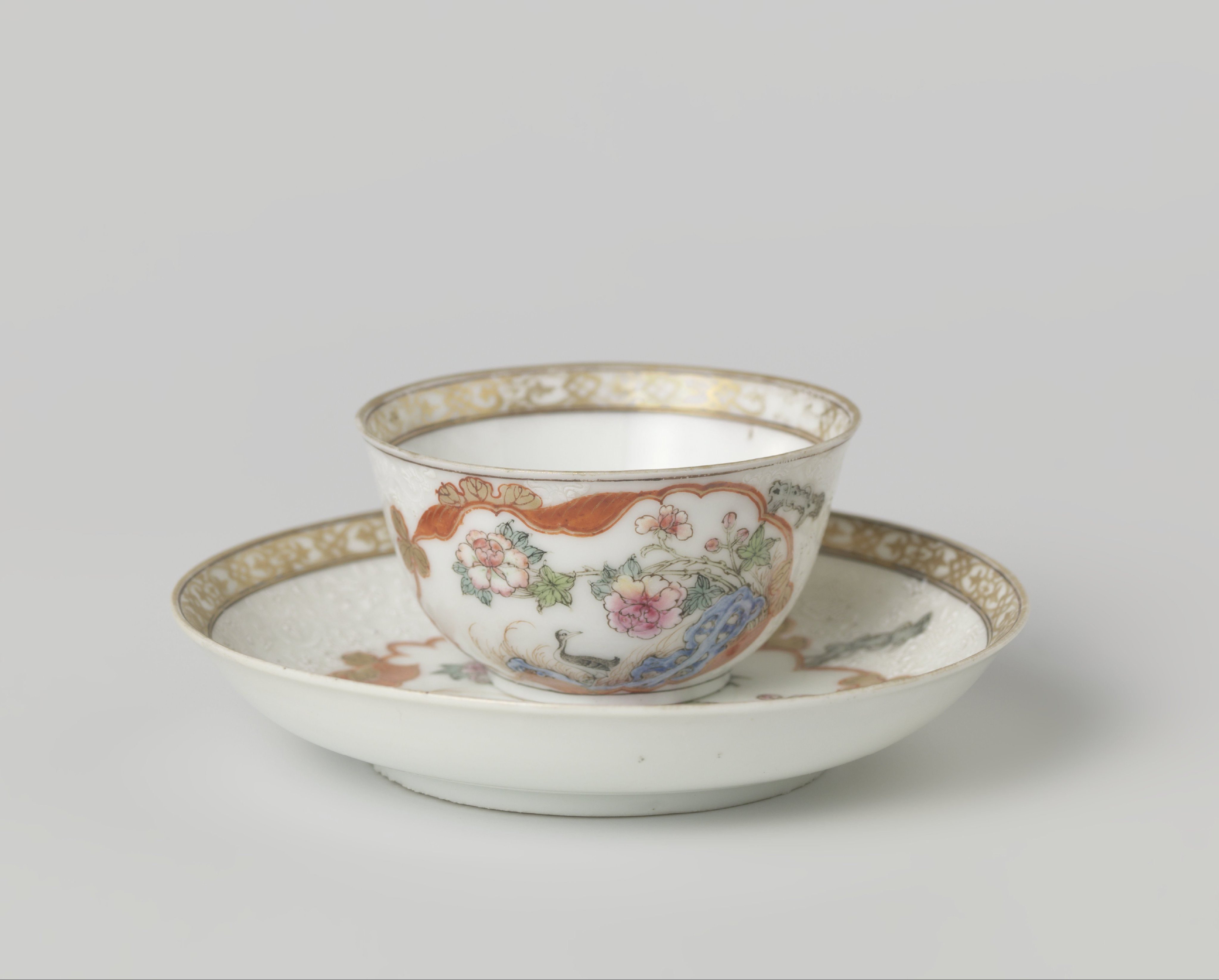 Bell-shaped cup and saucer with crane near a peony plant and rock