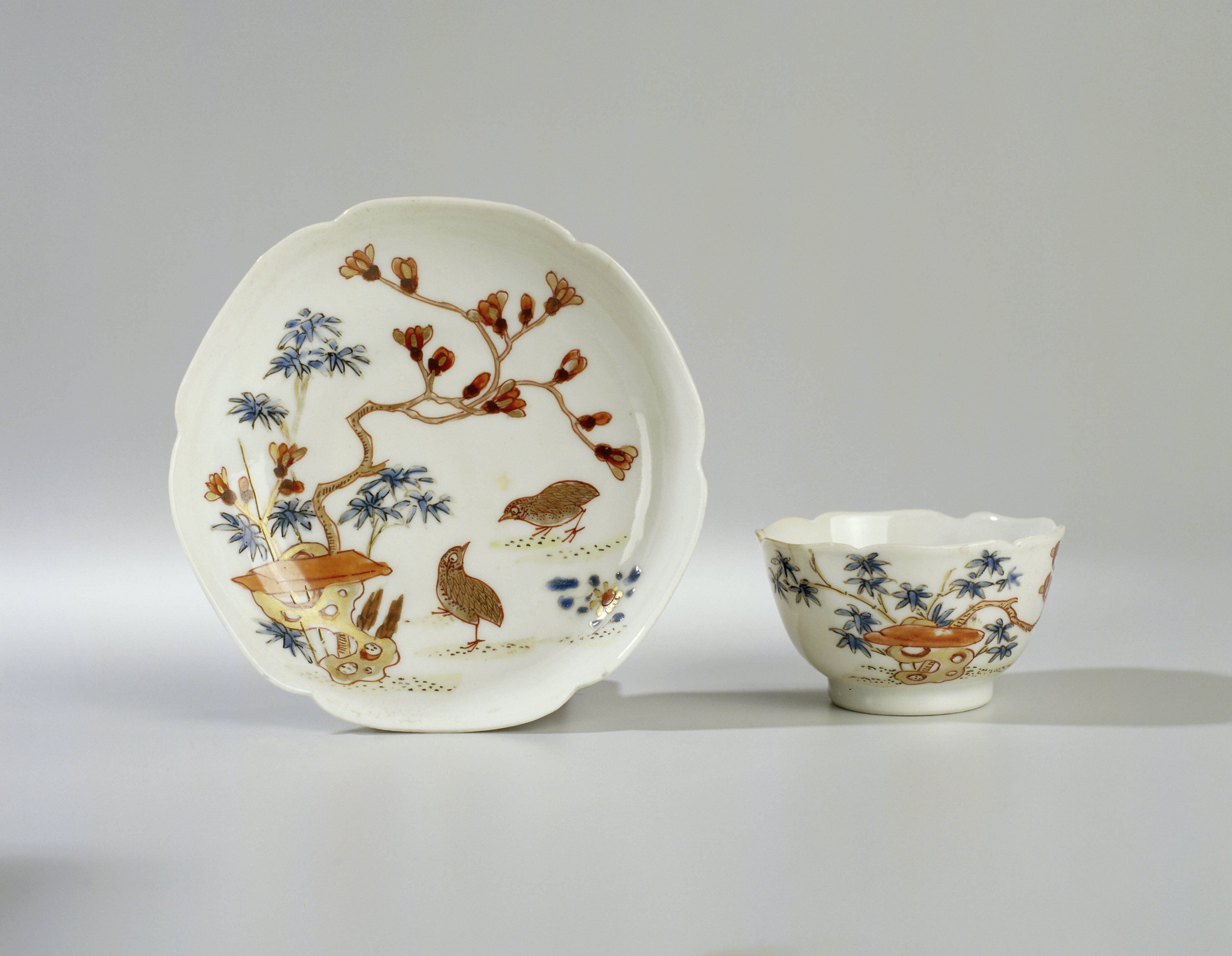 Bell-shaped cup and saucer with two quail near a rock