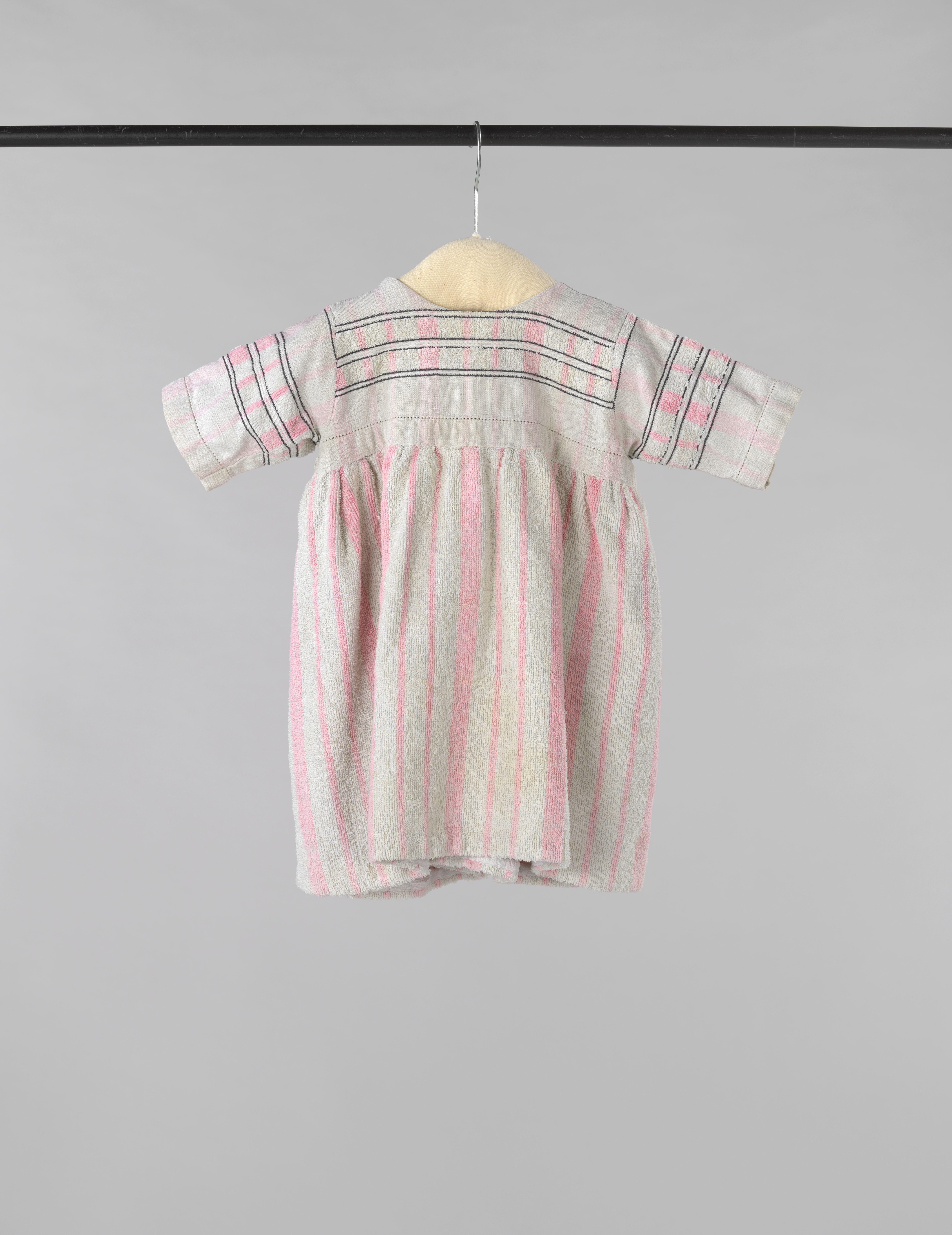 Kinderjurk met korte mouw, gemaakt van een wit-roze gestreepte badstoffen handdoek, op het lijf afgezet met zwarte siernaden
