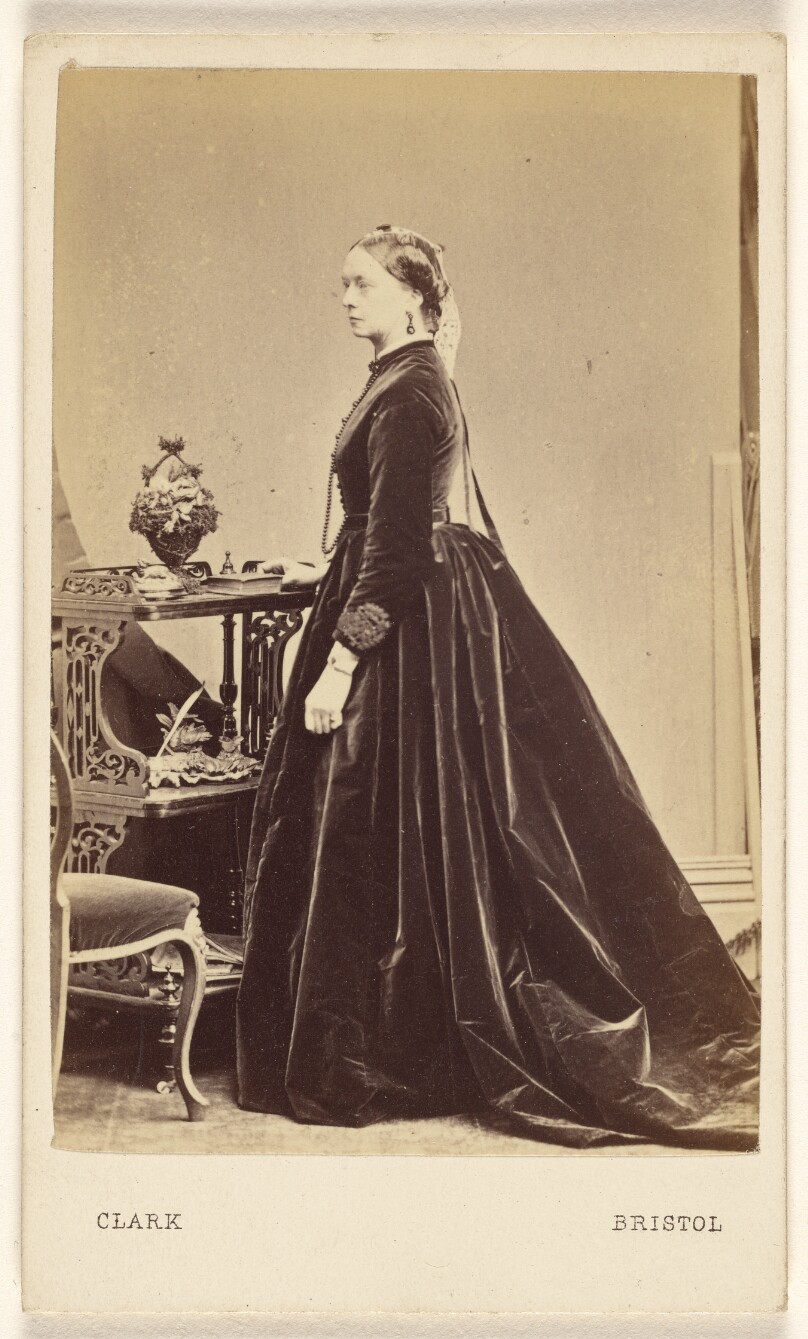 [Unidentified woman wearing a long dress, in profile, standing]