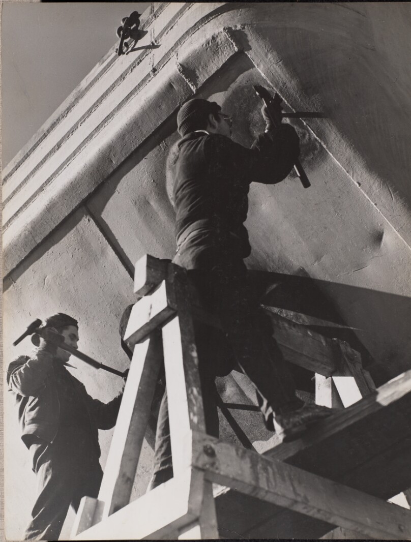 [Two men work on the underside of a boat]