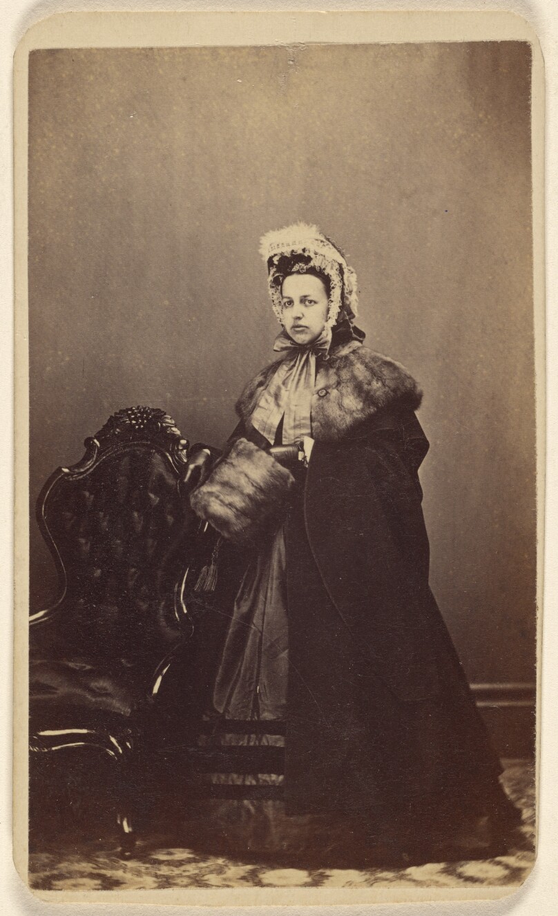 [Unidentified woman wearing an elegant outfit, complete with fur muff, standing]