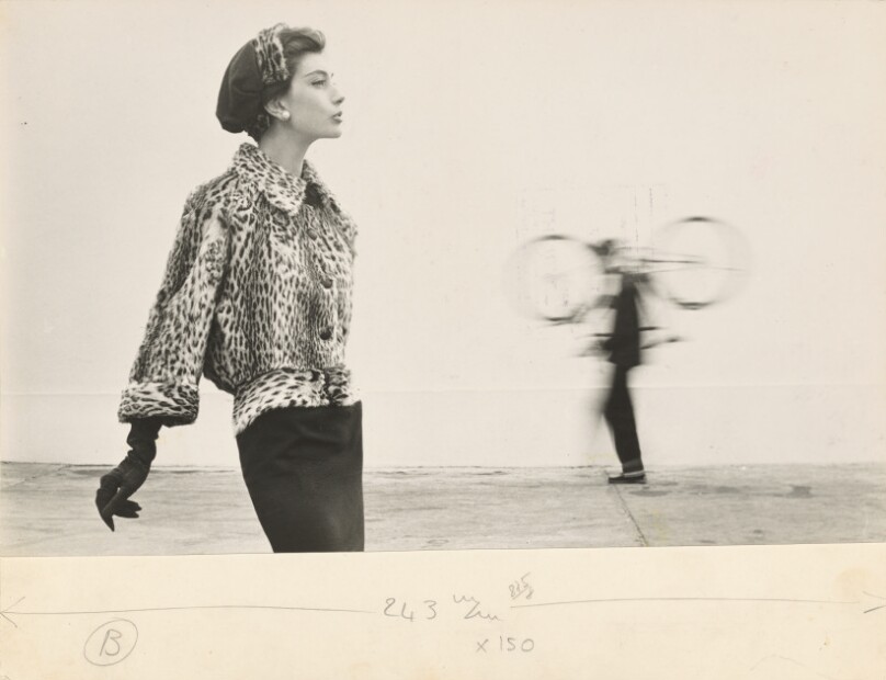 Model Wearing a Fur Coat and Gloves, Blurred Man Holding a Bicycle in the Background