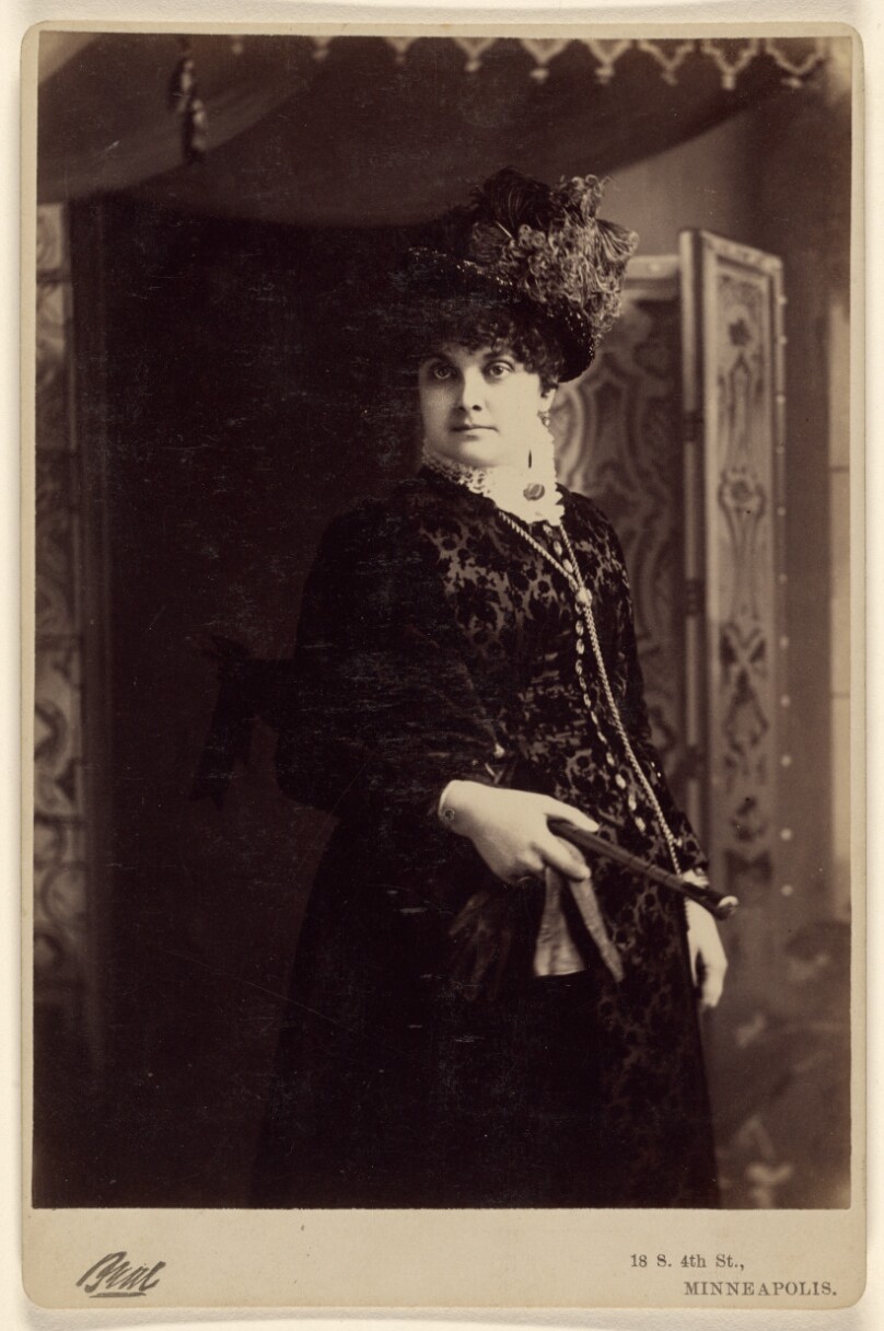 [Unidentified woman in fine dress and hat, standing]