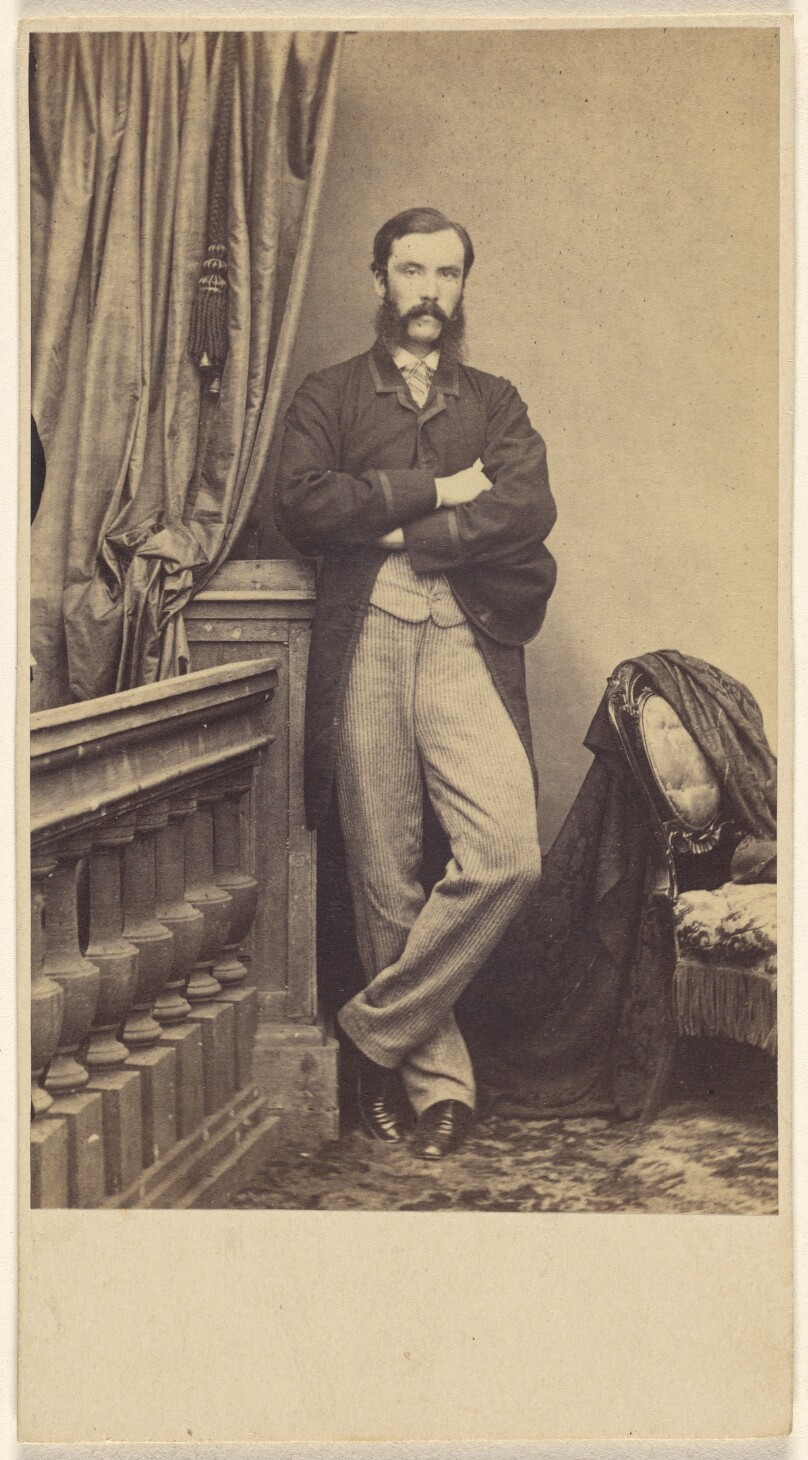 [Unidentified man with moustache & muttonchops, standing with arms crossed]