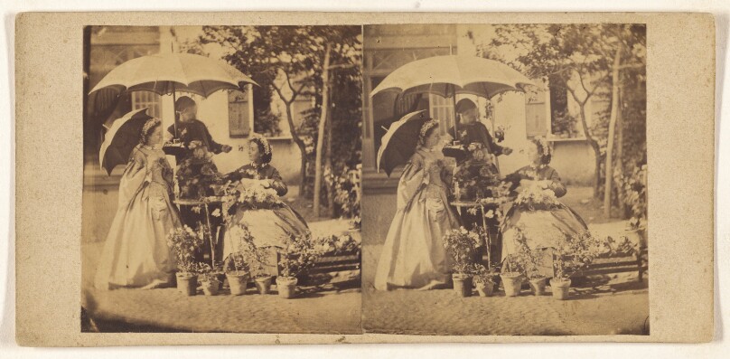 [Two ladies, one seated, one standing with a parasol, being served tea at a table under a large umbrella by a man wearing a cap]