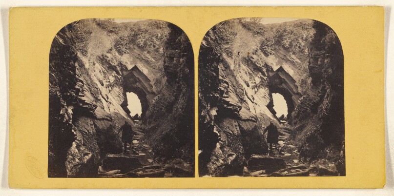 [Man standing within jagged rocks, hole at center]