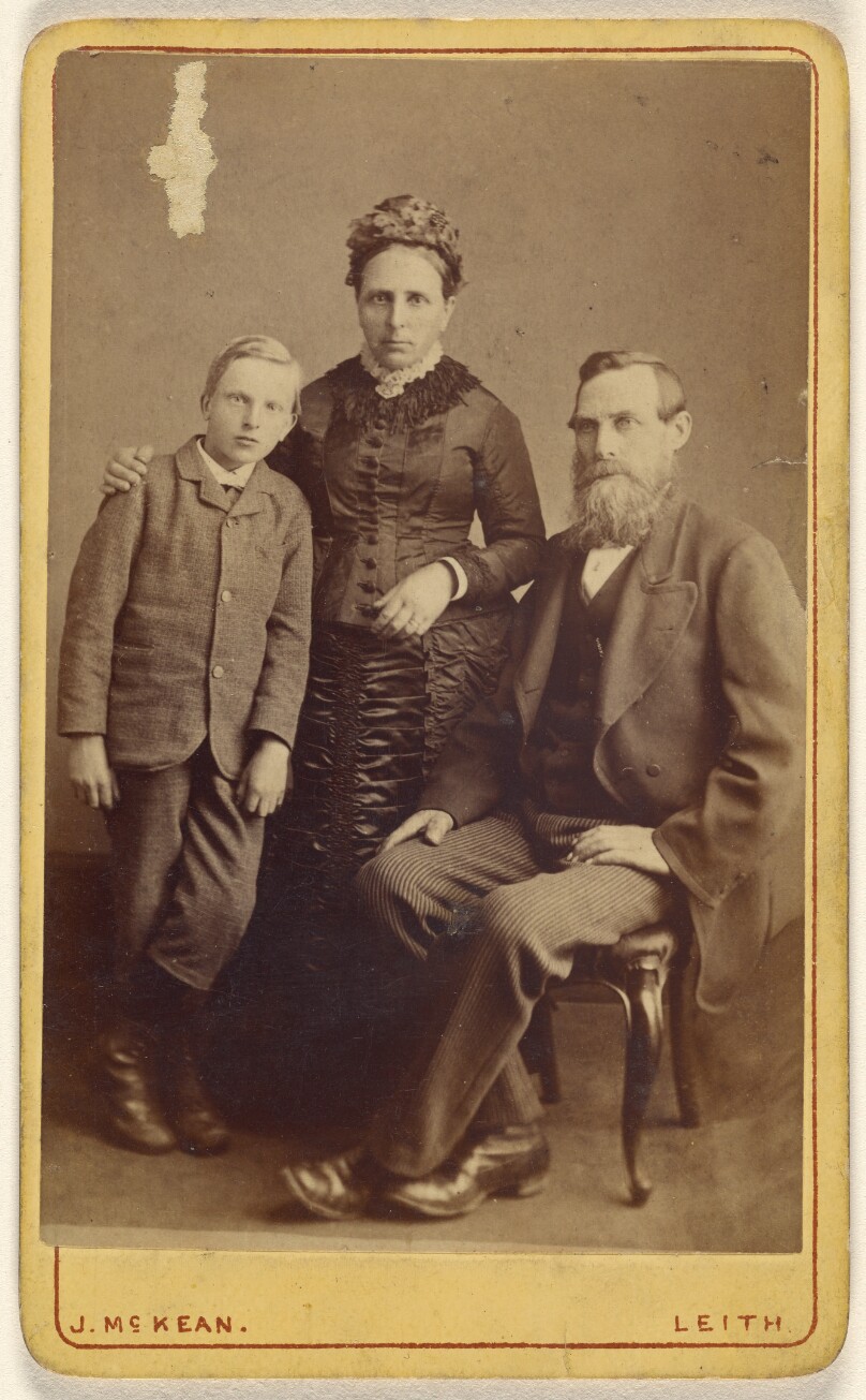 [Portrait of an unidentified family: mother and son standing, bearded father seated]