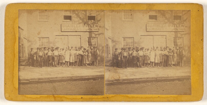 [Group of people posed in front of building of Shaible & Butler Carriage & Sleigh Factory]