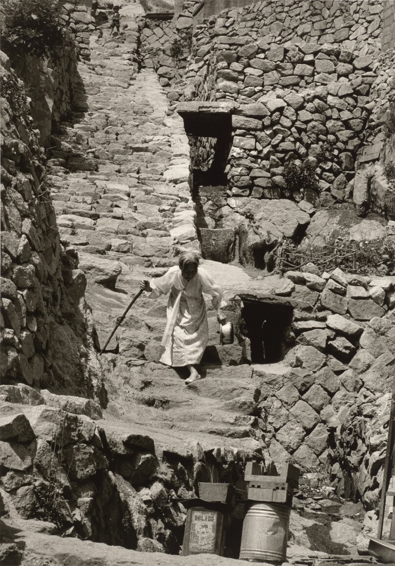 [Elderly Woman Climbing Down Stone Stairs with a Walking Stick]