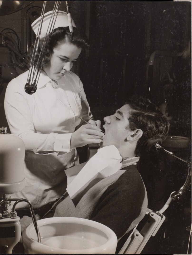 [Dental hygienist inspects a patient's mouth]