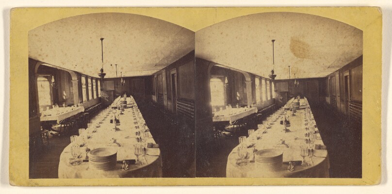 [Interior of a dining hall, large table with full place settings]