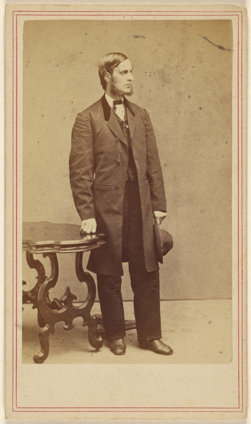 [Unidentified man with long muttonchops standing, holding his hat in his left hand]