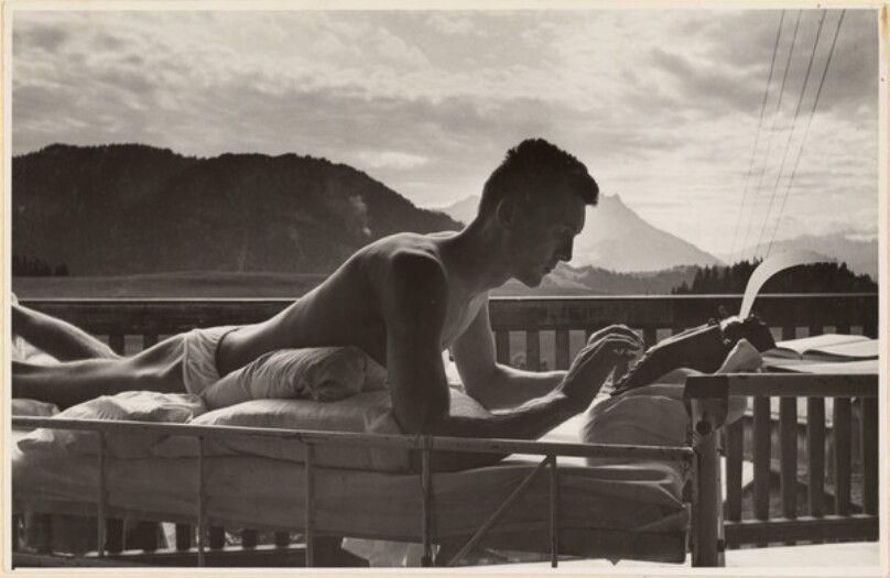 [Man using typewriter on bed]