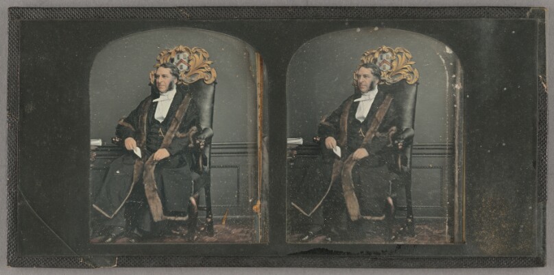 [Seated man with muttonchop whiskers in robes, on crested chair]