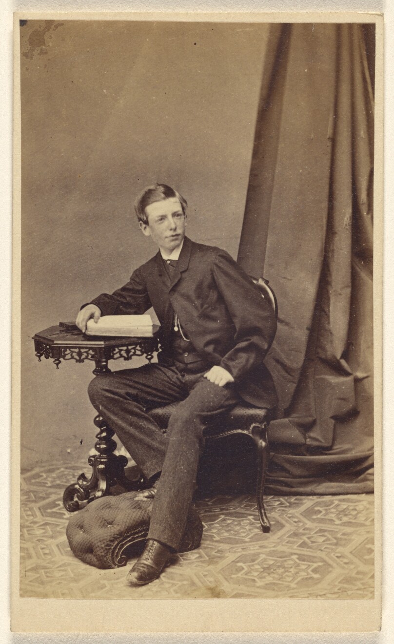 [Unidentified young man seated at a table with a book on top]