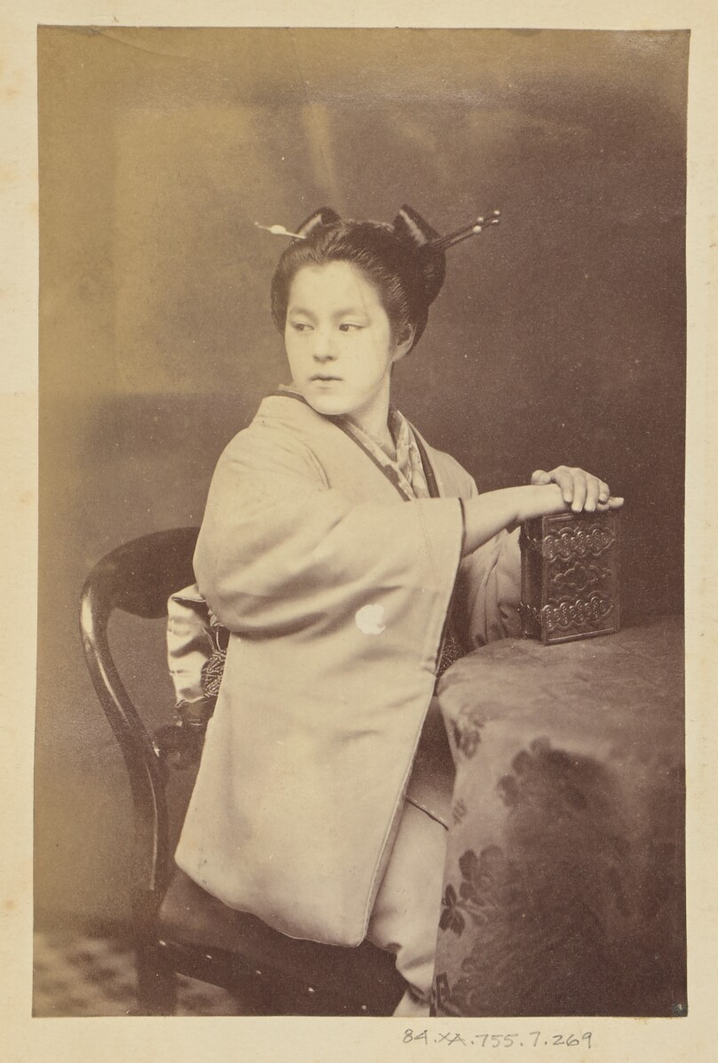 [Seated Japanese woman holding a cartes-de-visite album at a table]