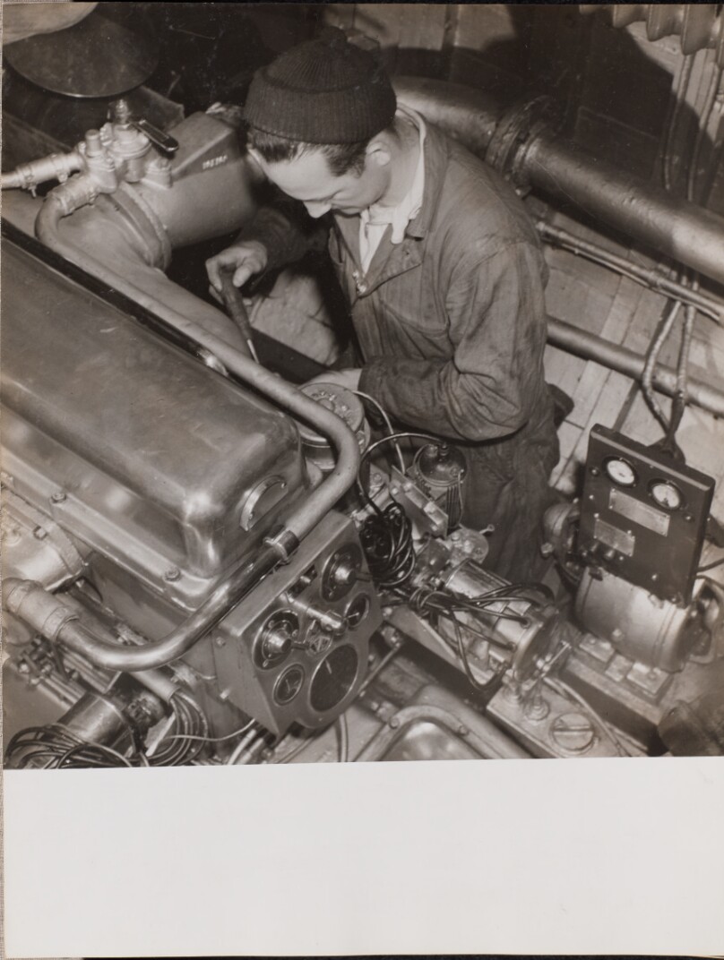 [Man wearing a knit cap works on an engine]