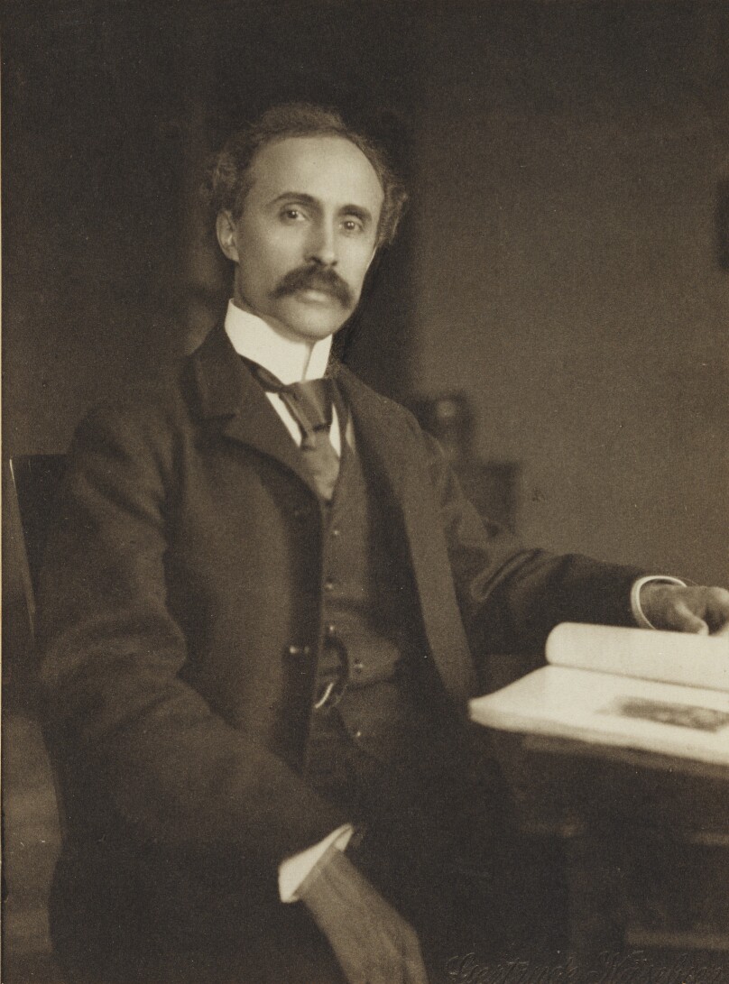 [Man seated with table and book]