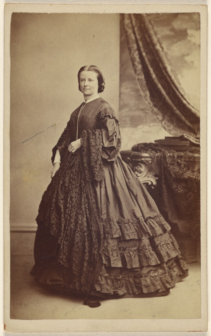 [Unidentified woman wearing a long dark dress, standing]
