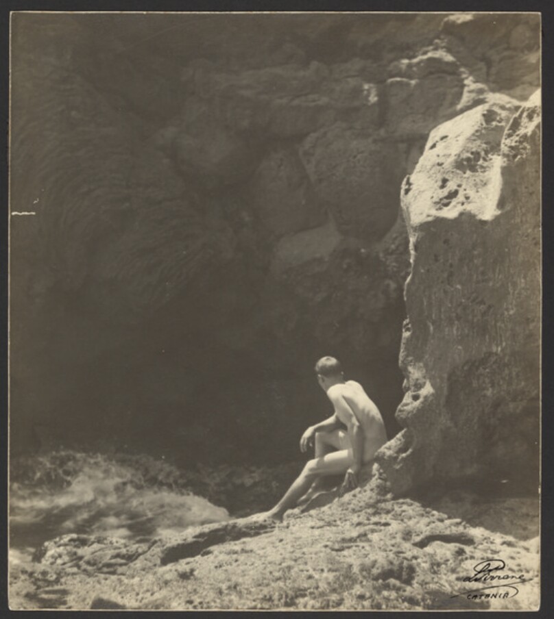 [Man seated at base of cliffs]