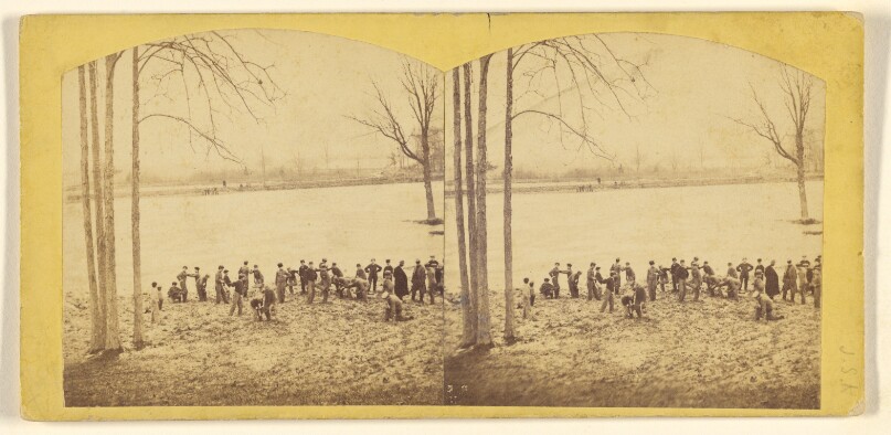 [Large group of men at open field with barren trees, lake in background]