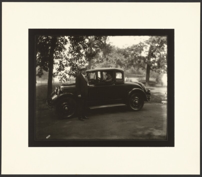 [Man standing beside car driven by woman]