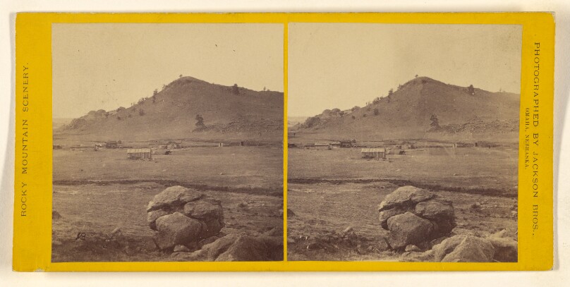 [Long view of cabin on plain, rock formation at foreground]